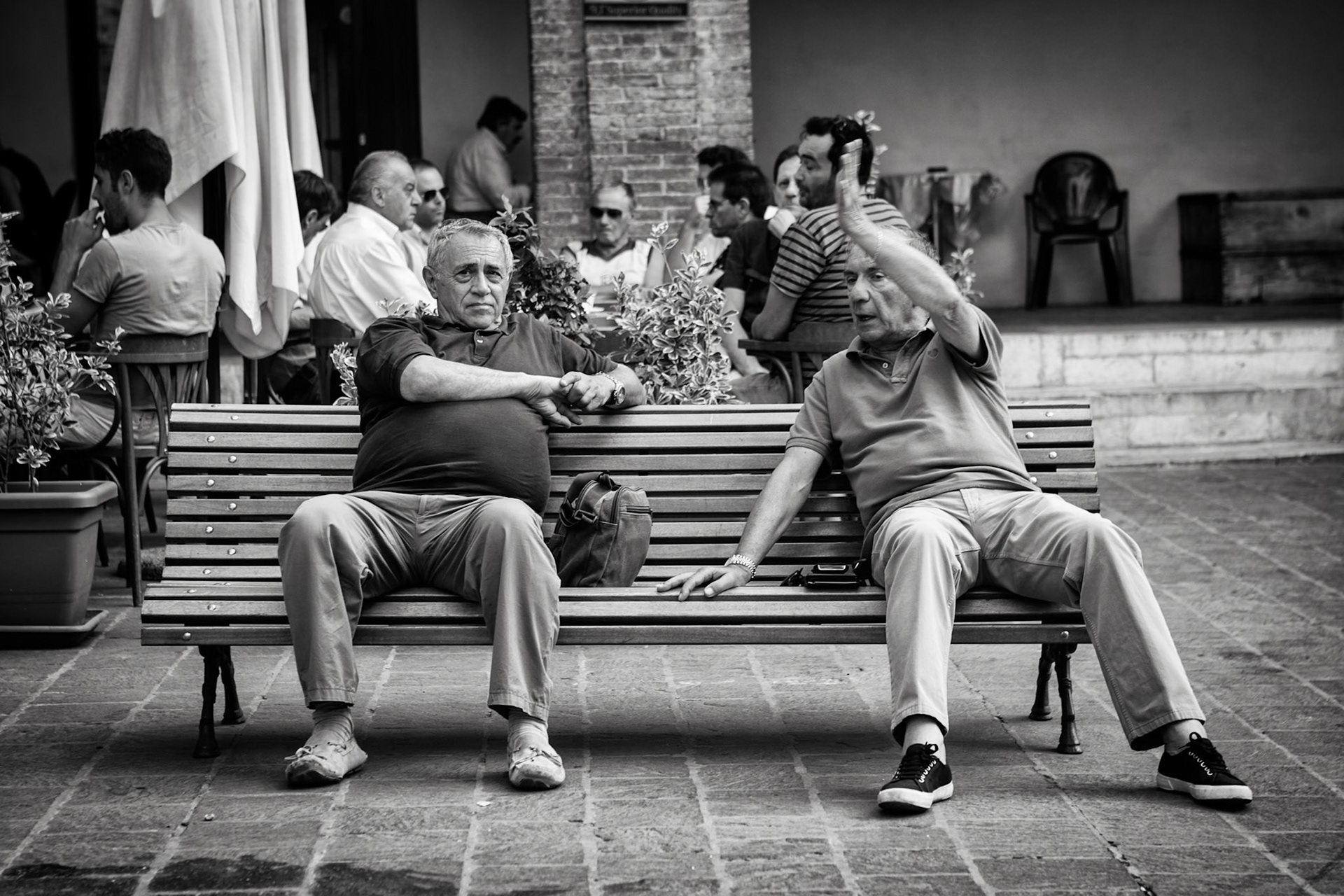 Gubbio, Italy - July 31st 2012 : Two men on a bench in an active conversation.  Typical italian gestures. In the background men are drinking coffee and playing cards. [url=http://www.istockphoto.com/search/lightbox/11293042#64eec1d][img]http://www.piebinga.nl/banners/italy.jpg[/img][/url]