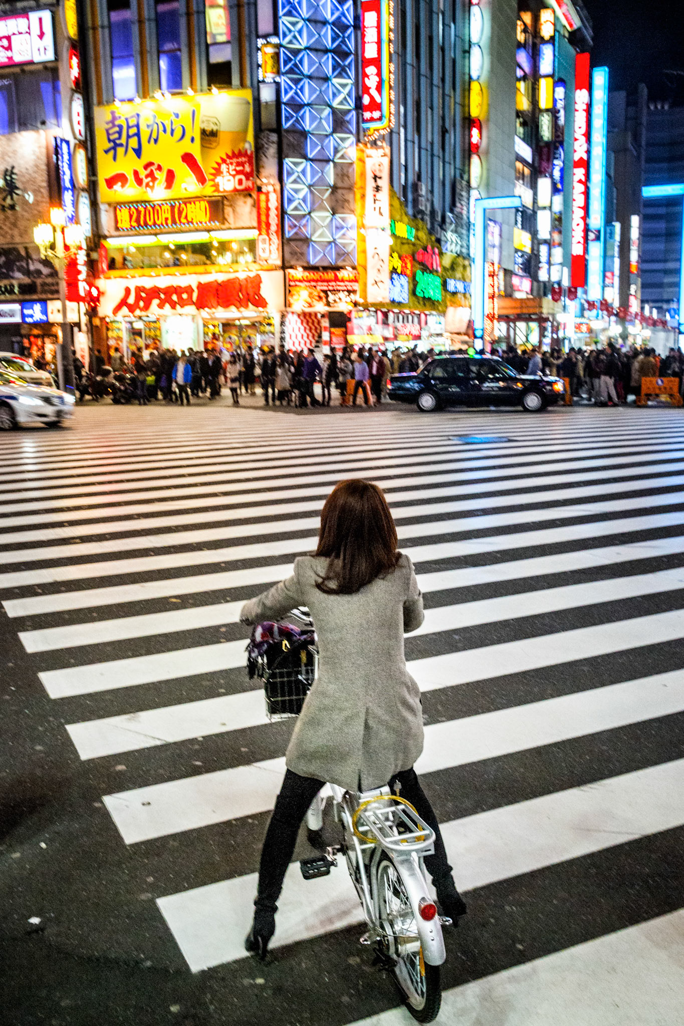 Tokyo, Japan - April 11, 2015 : Girl with bicycle, seen from behind, at  tokyo zebra crossing, crowd and neon light in the background