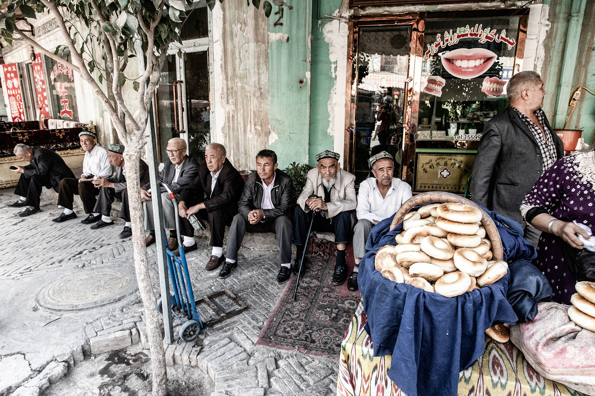 Kashgar,  China - September 11th, 2018 : Uyghur men relaxing near a bakery, nan bread in the foreground.