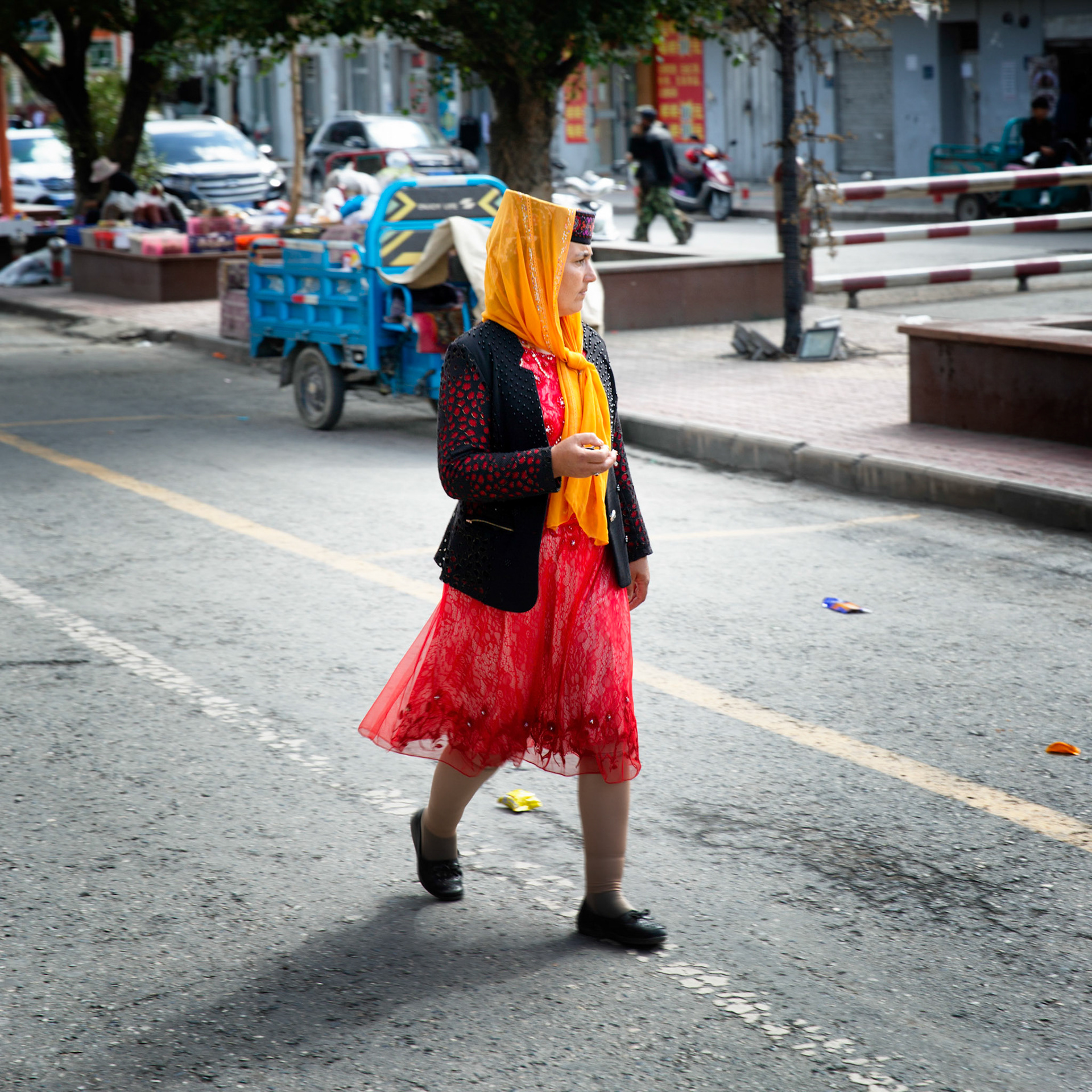 Tashgurkan, China - September 7th, 2018 : Woman wearing typical dress for the area, crossing the road in Tashgurkan.