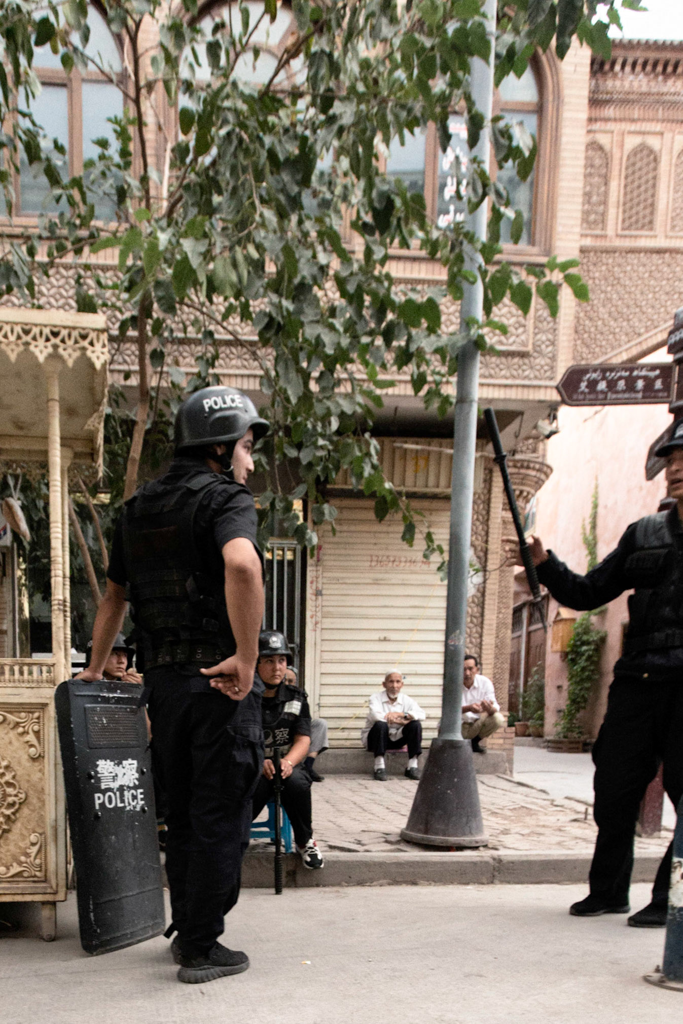 Kashgar,  China - September 11th, 2018 : Police patrol taking a rest and chatting at a food stall in the Kashgar food market, uyghur people in the background.