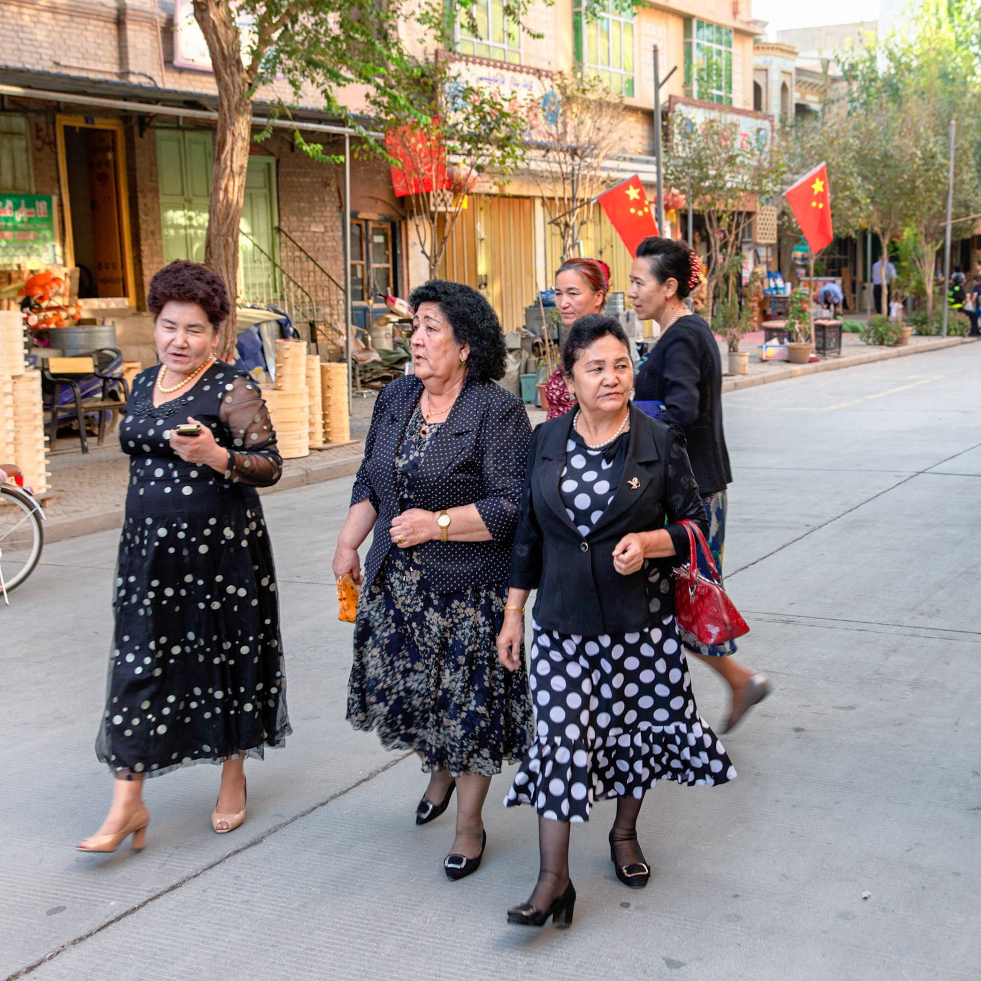 Kashgar,  China - September 8th, 2018 : Group of women walking the streets in the Kashgar old town, many chinese flags hanging from the houses and shops.