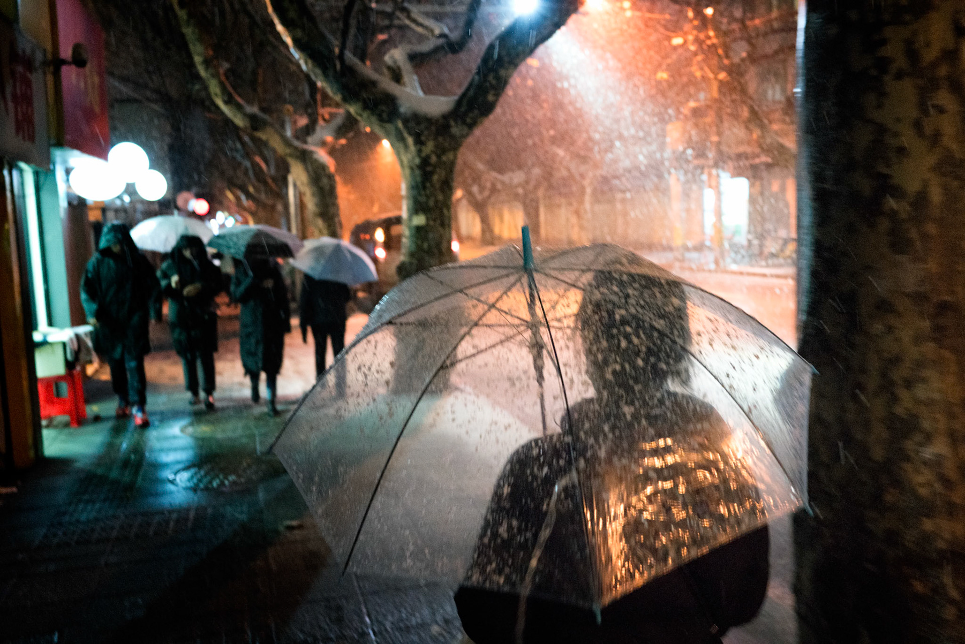 Shanghai, China - January 25th 2018 : Evening image of people carrying umbrellas in a wet snowy evening