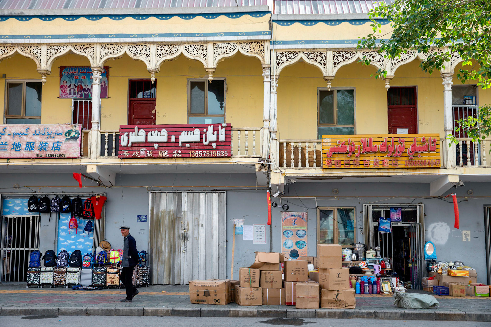 Tashgurkan, China - September 7th, 2018 : Man walking in front of a shop in Tashgurkan, note the arab and chinese language signs.