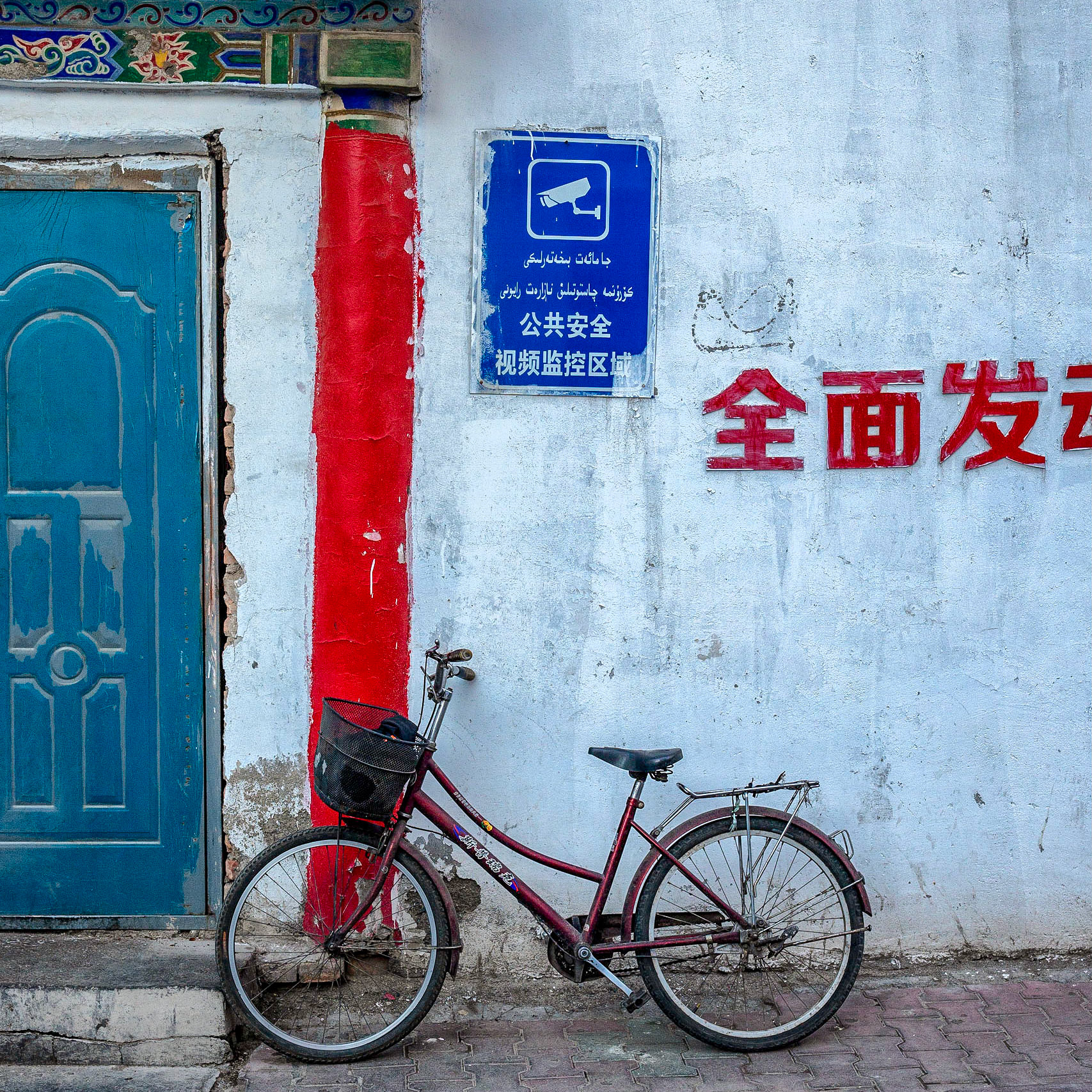 Urumqi, China - september 1, 2018 : bicycle parked against a wall, under a sign telling, in both arab as well as chinese language, people there is security camera surveillance