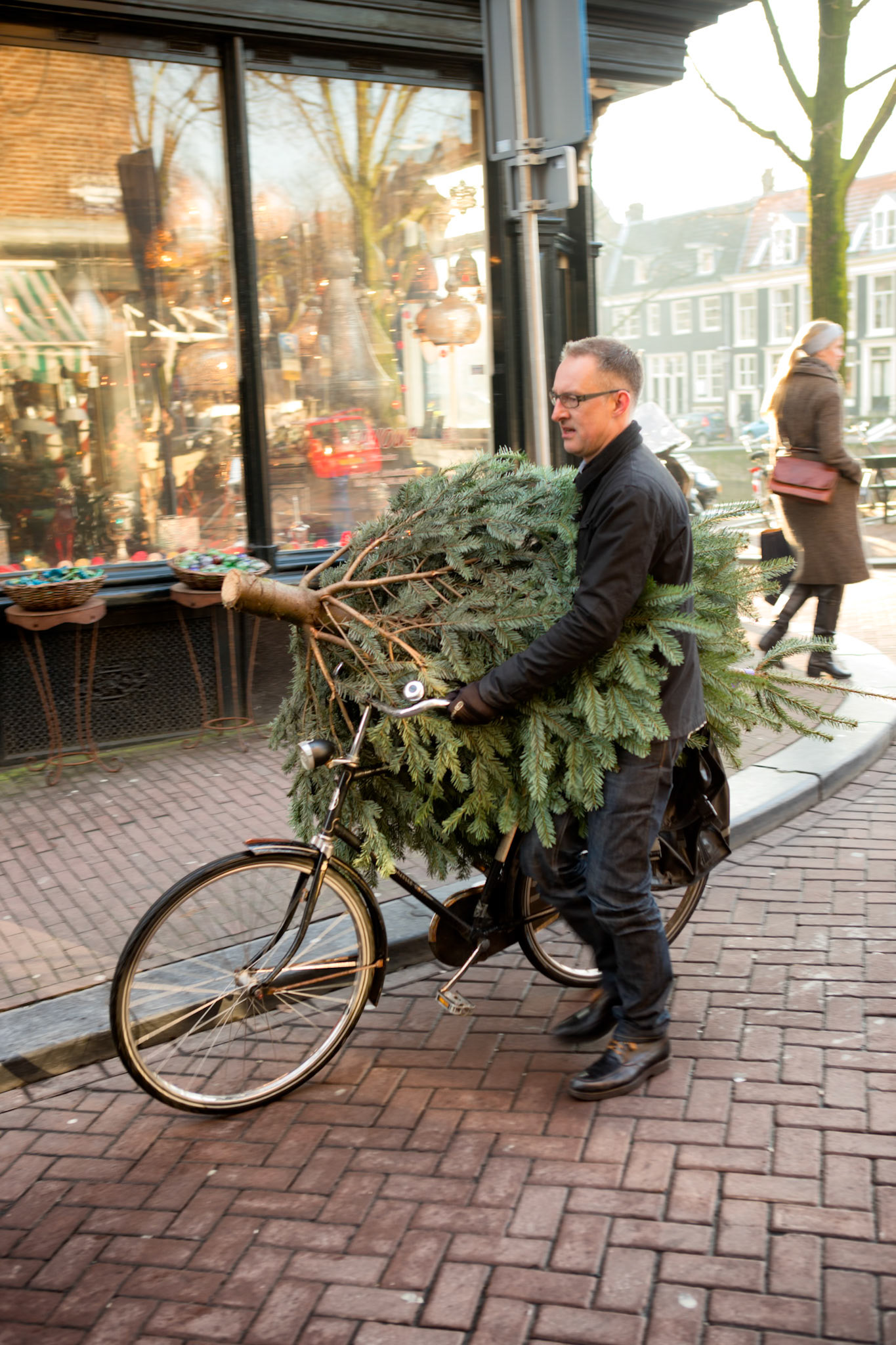 Amsterdam, the Netherlands - December 8th, 2012 : Man transporting a cut christmas tree on his bicycle in a street in Amsterdam. People and shopfronts in the background [url=http://www.istockphoto.com/search/lightbox/11479058#17a1cde8][img]http://www.piebinga.nl/banners/holland.jpg[/img][/url]