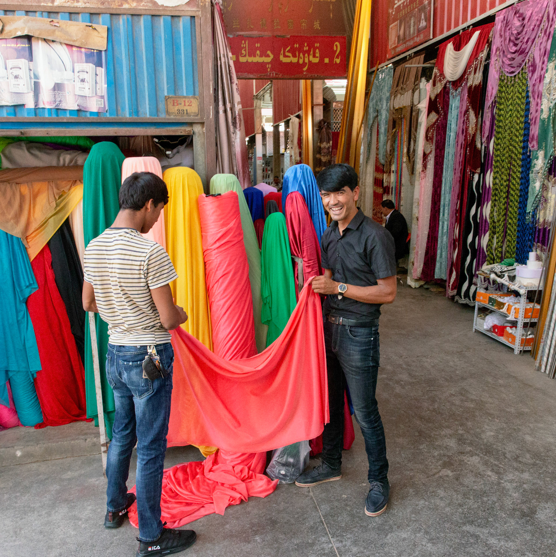 Kashgar,  China - September 10th, 2018 : Two men holding textile a their shop in the Kashgar grand bazaar.