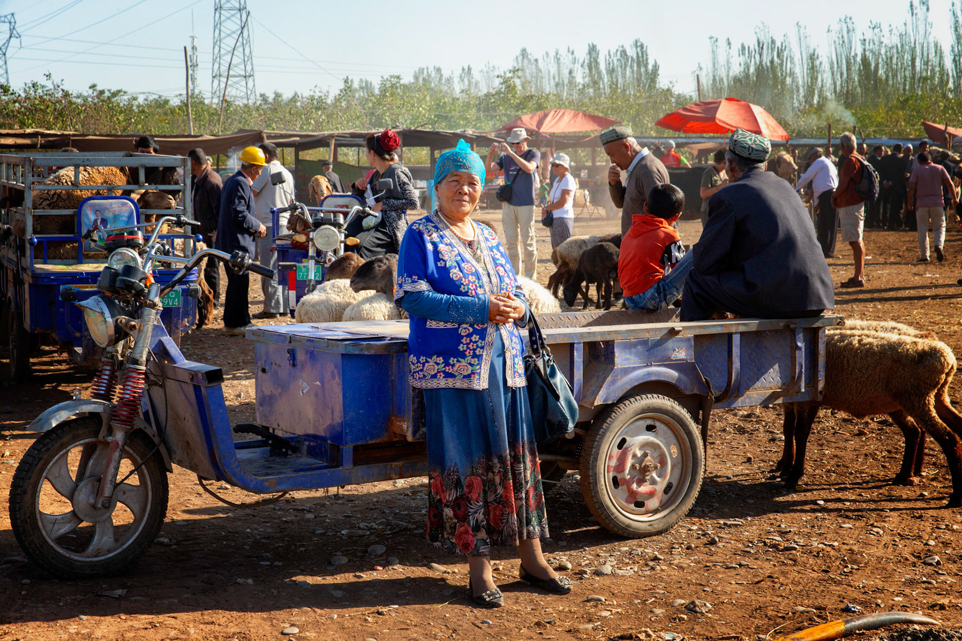 Kashgar,  China - September 9th, 2018 : Woman leanding against a small 3-wheel transport at the Kashgar sunday cattle market. Man sitting in the back, people and animals in the background
