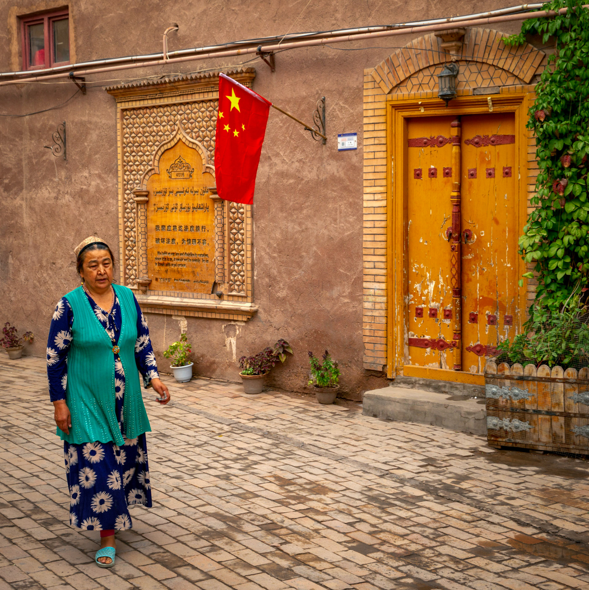 Kashgar, Xinjiang, China - September 5, 2018: Woman walking in one of the rebuilt streets in Kashgar Old City. CHinese flag on te wall and inscriptions in both chinese as well as arab/uyghur language.