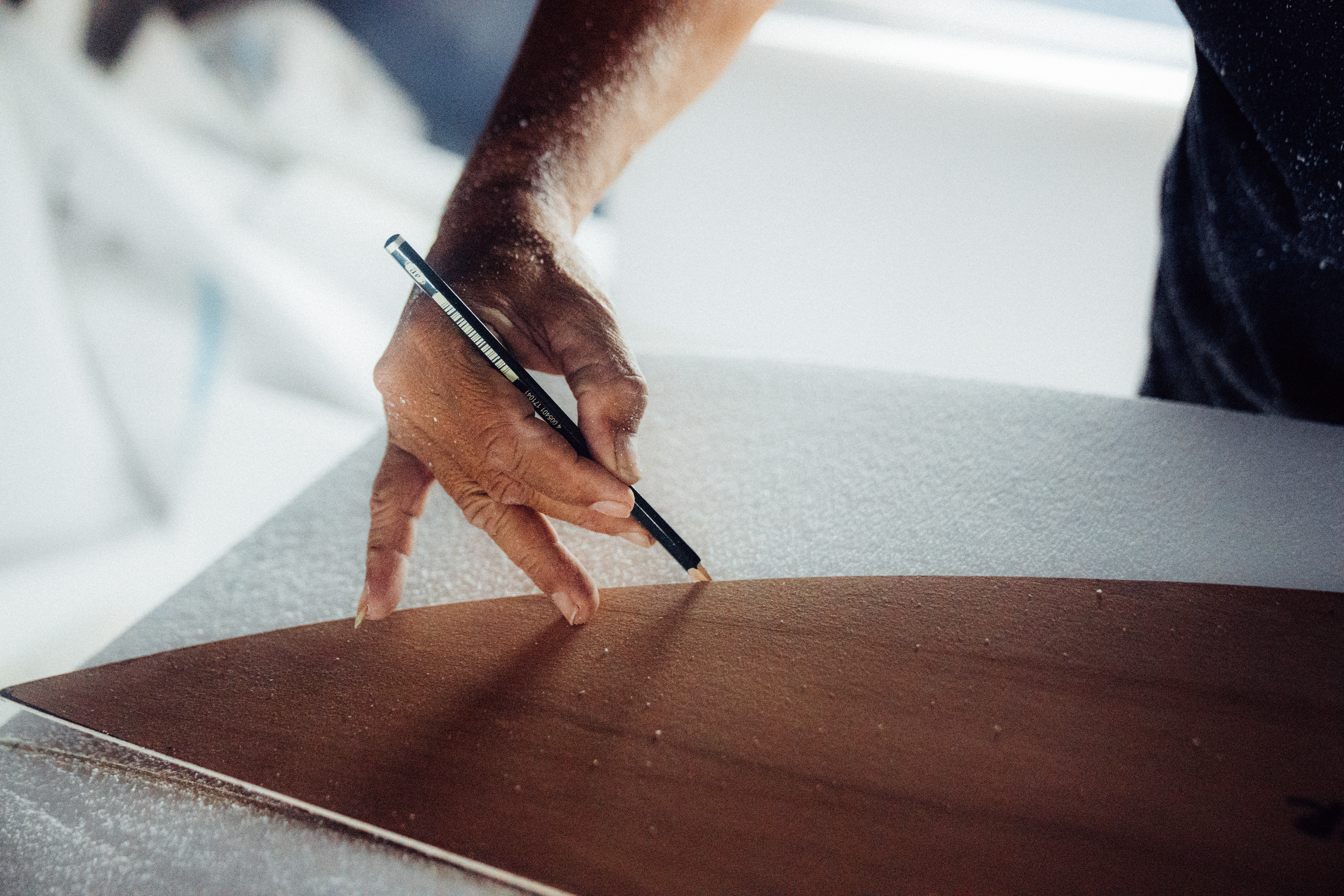 Nahaufnahme eines Handwerkers, der mit einer Schablone die perfekte Outline eines Surfboards zeichnet.