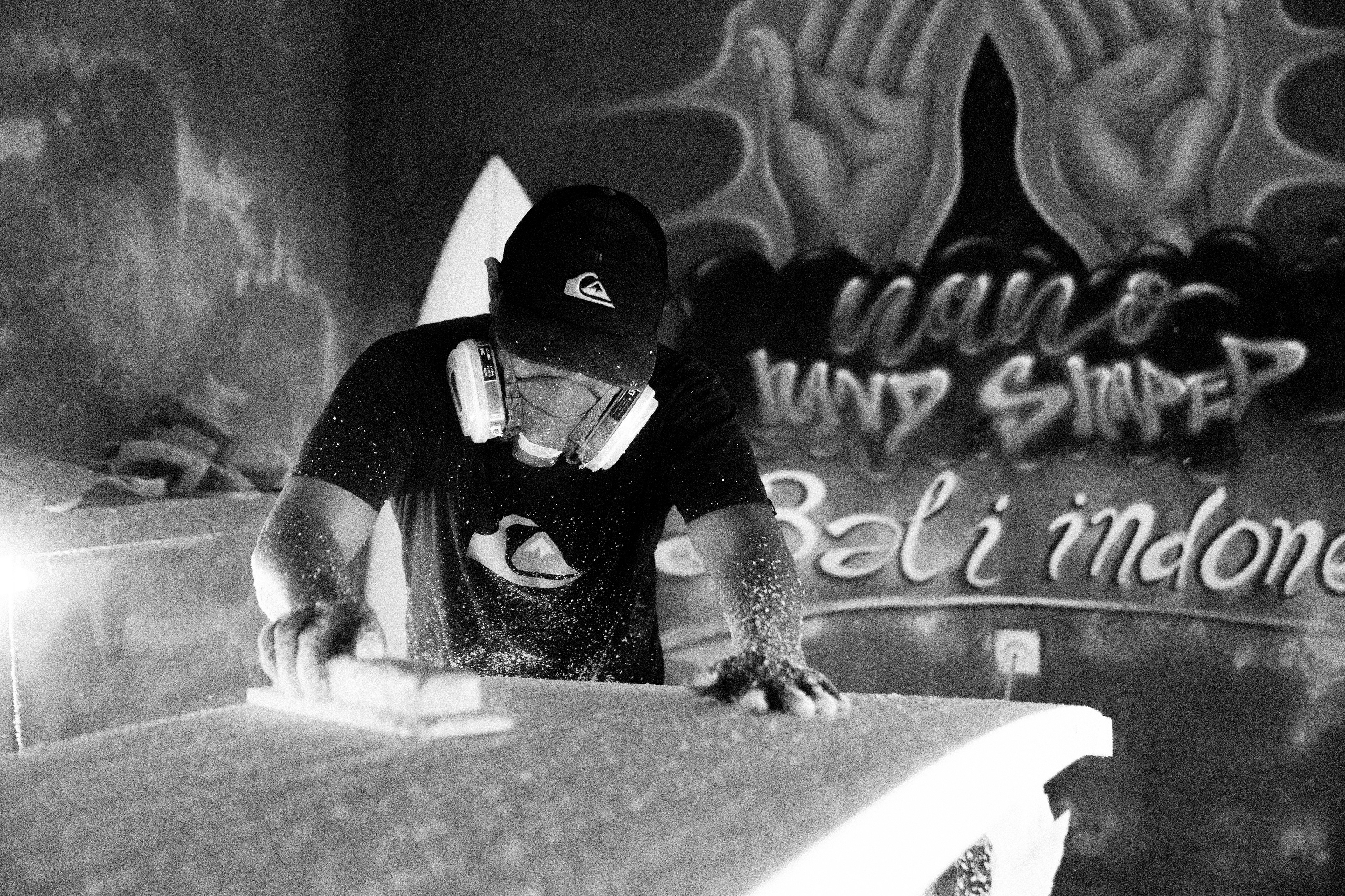Ein Shaper auf Bali schleift mit einem Block die feinen Konturen eines Surfboards von Hand.