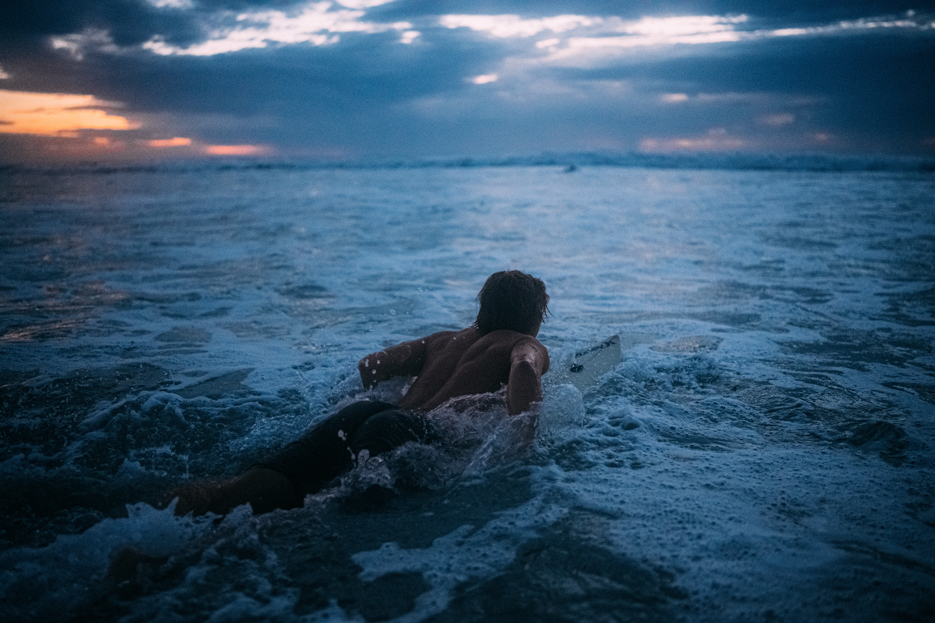 Leuchtende Wellen brechen im letzten Licht des Tages, ein Surfer verschmilzt mit der Szenerie.