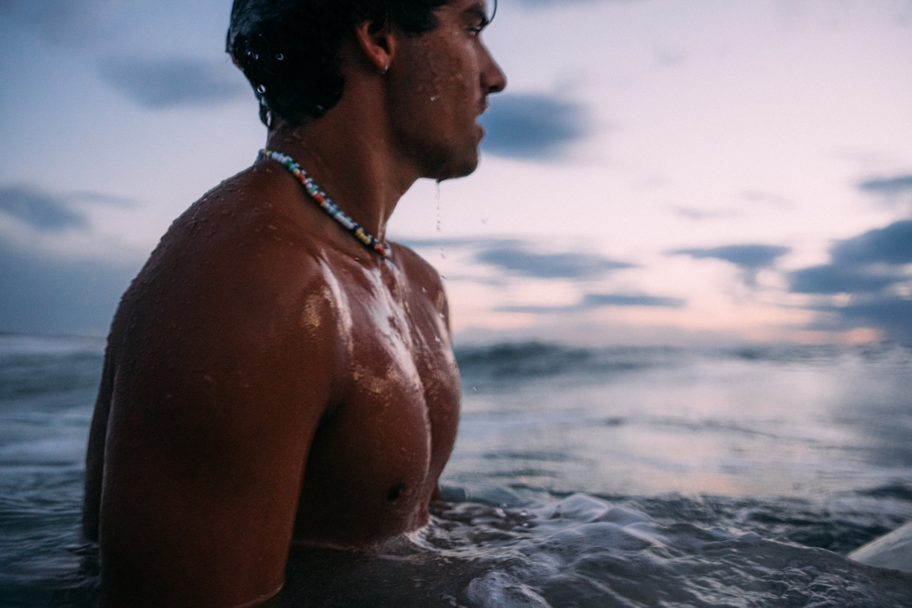 Surfer sitzt auf seinem Board im Ozean, umgeben von den weichen Farben der Blauen Stunde.
