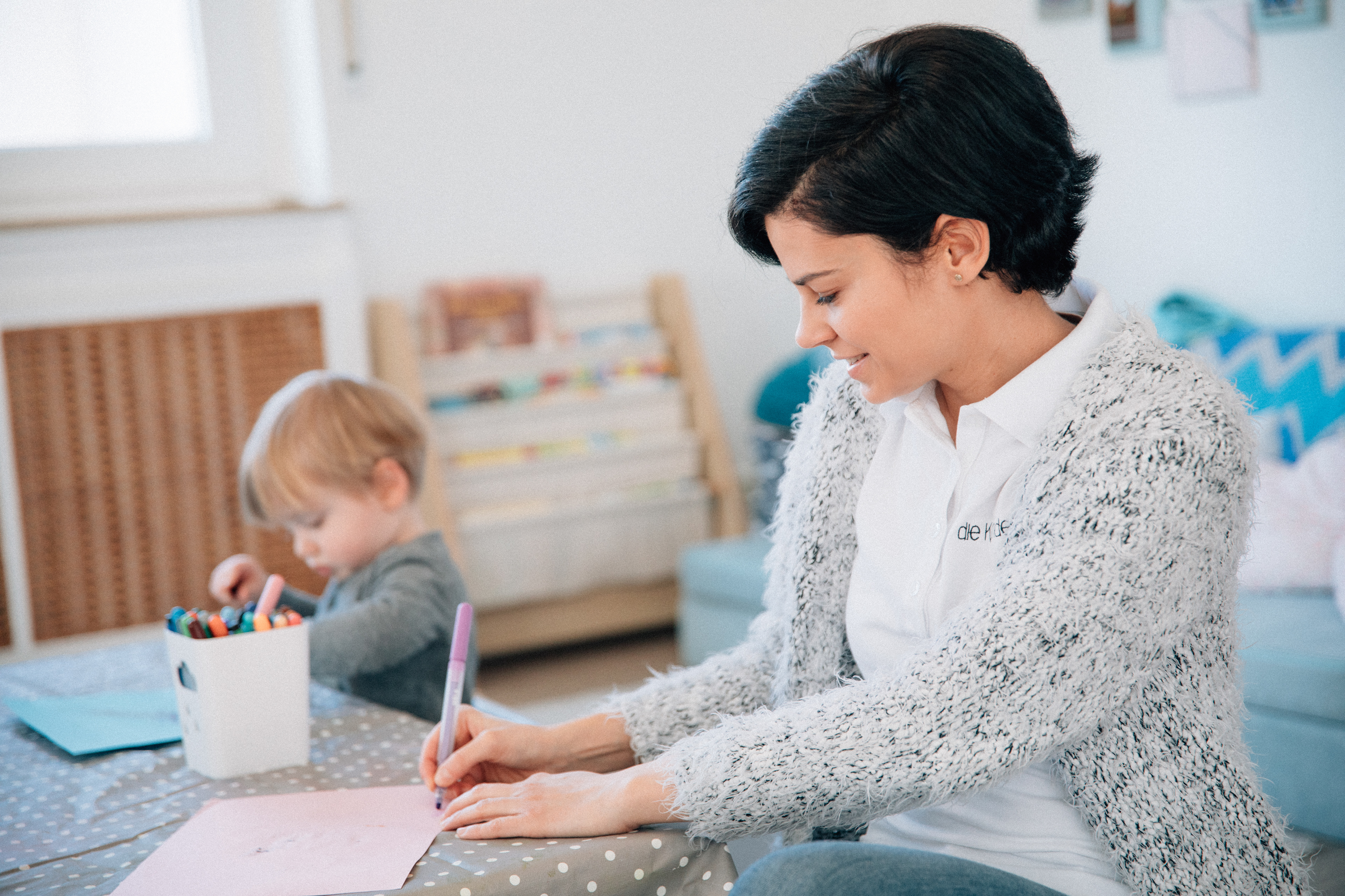 Eine einfühlsame Erzieherin betreut lachende Kinder in der Kindervilla Stuttgart.