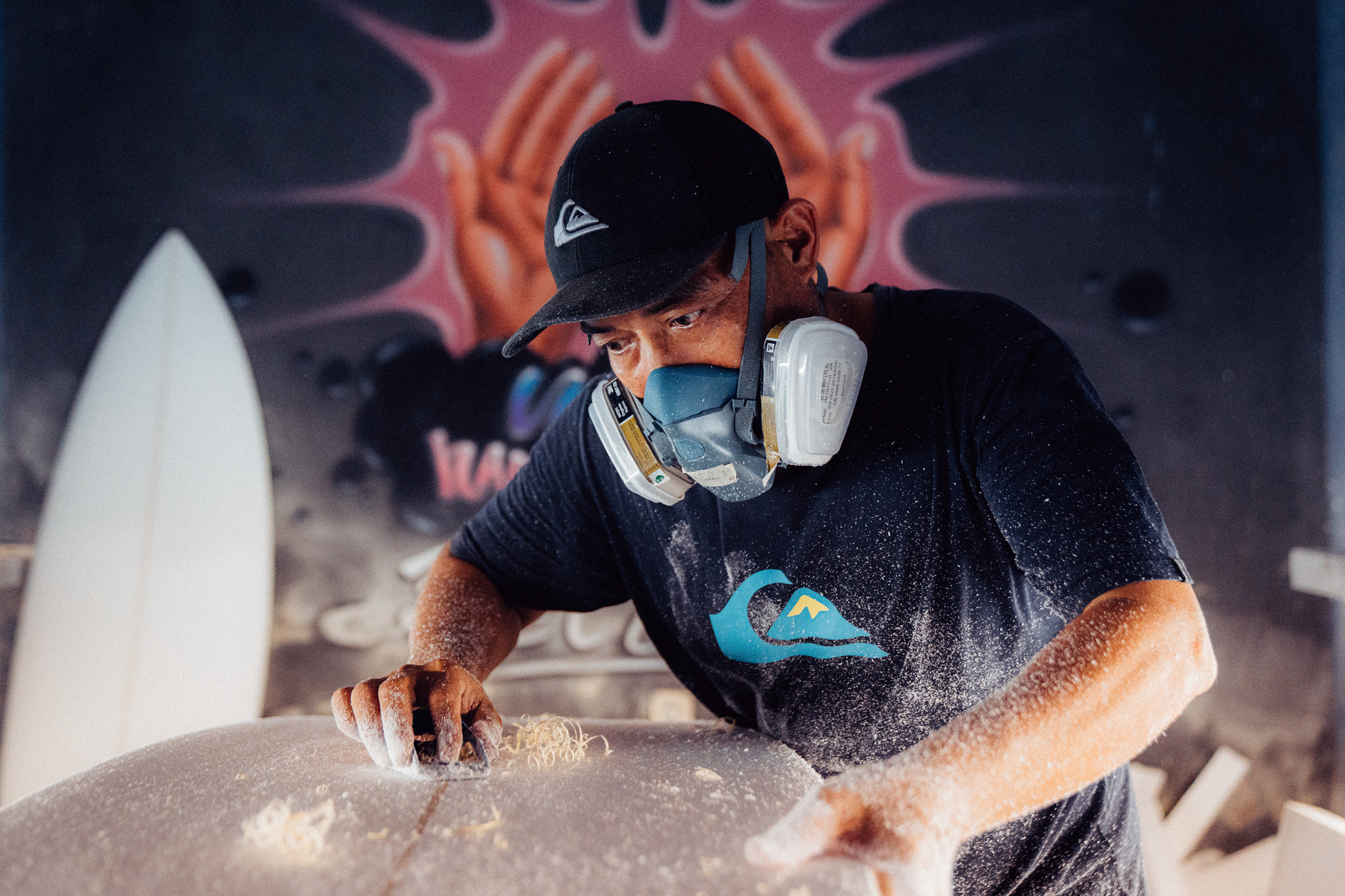 Ein balinesischer Surfboard-Shaper glättet mit einem Schleifblock vorsichtig die Rails eines neuen Boards.