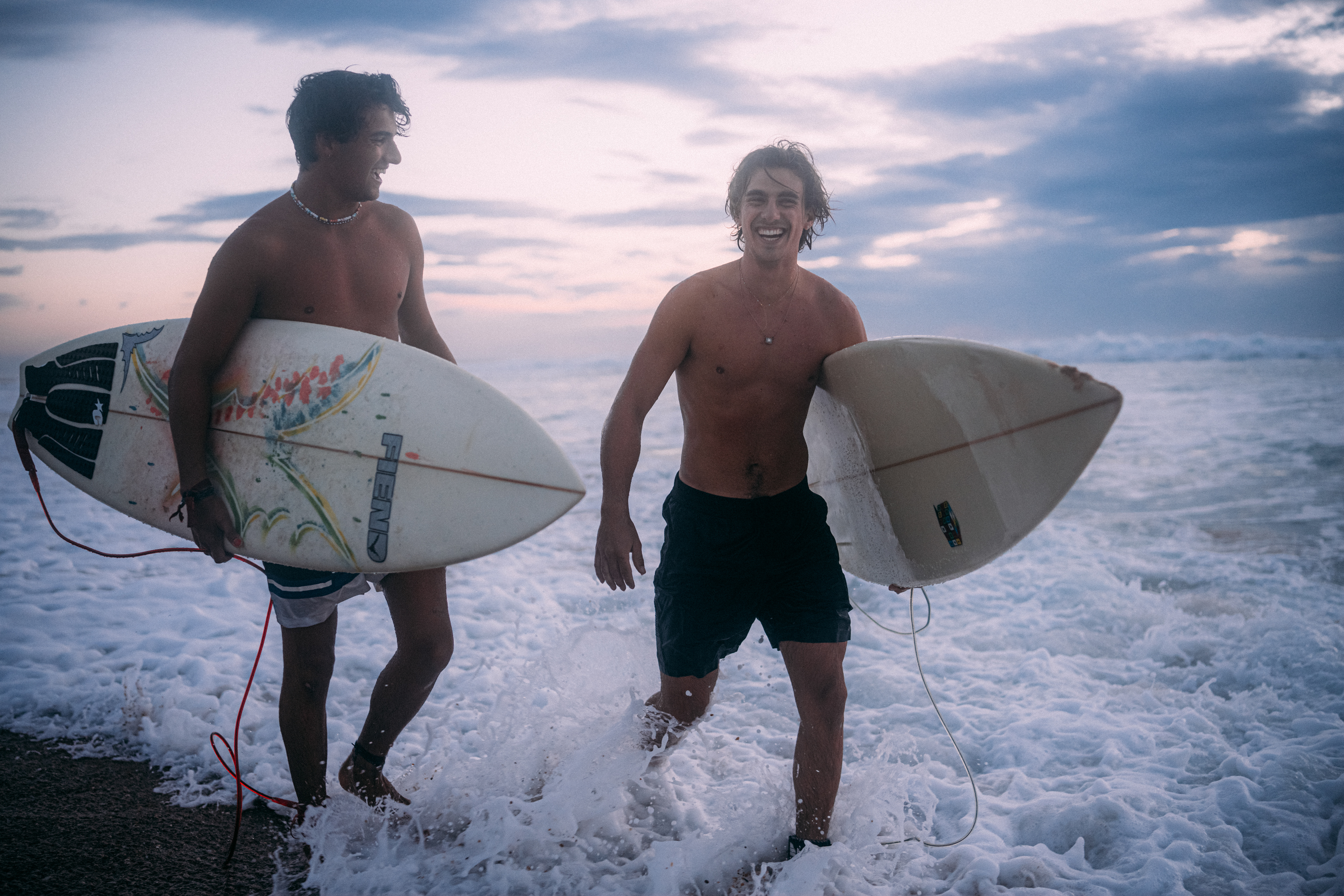 Silhouette eines Surfers auf einer Welle, umgeben von den sanften Blautönen der Abenddämmerung.
