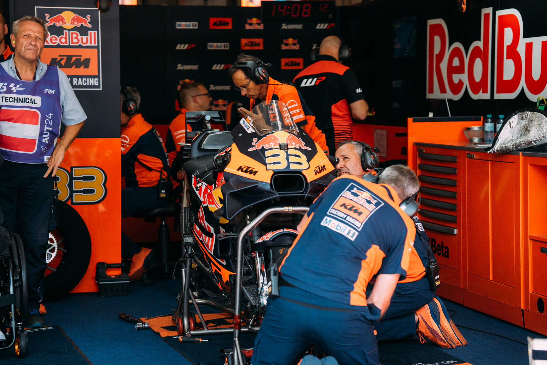 MotoGP-Fahrer in AlphaTauri-Rennbekleidung neben einem Rennmotorrad in einer urbanen Umgebung.
