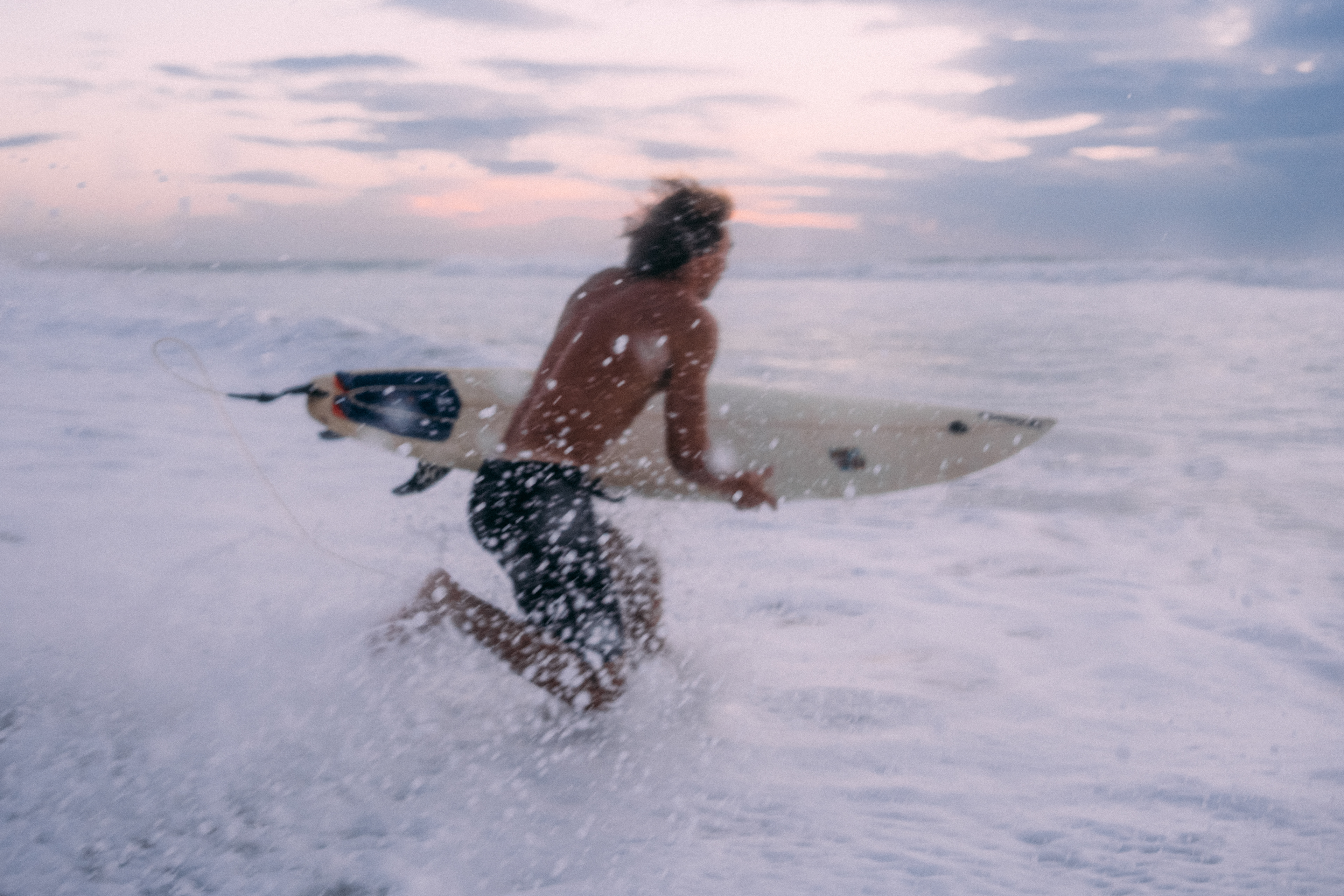 Die letzten Sonnenstrahlen spiegeln sich auf dem Wasser, während ein Surfer elegant eine Welle nimmt.