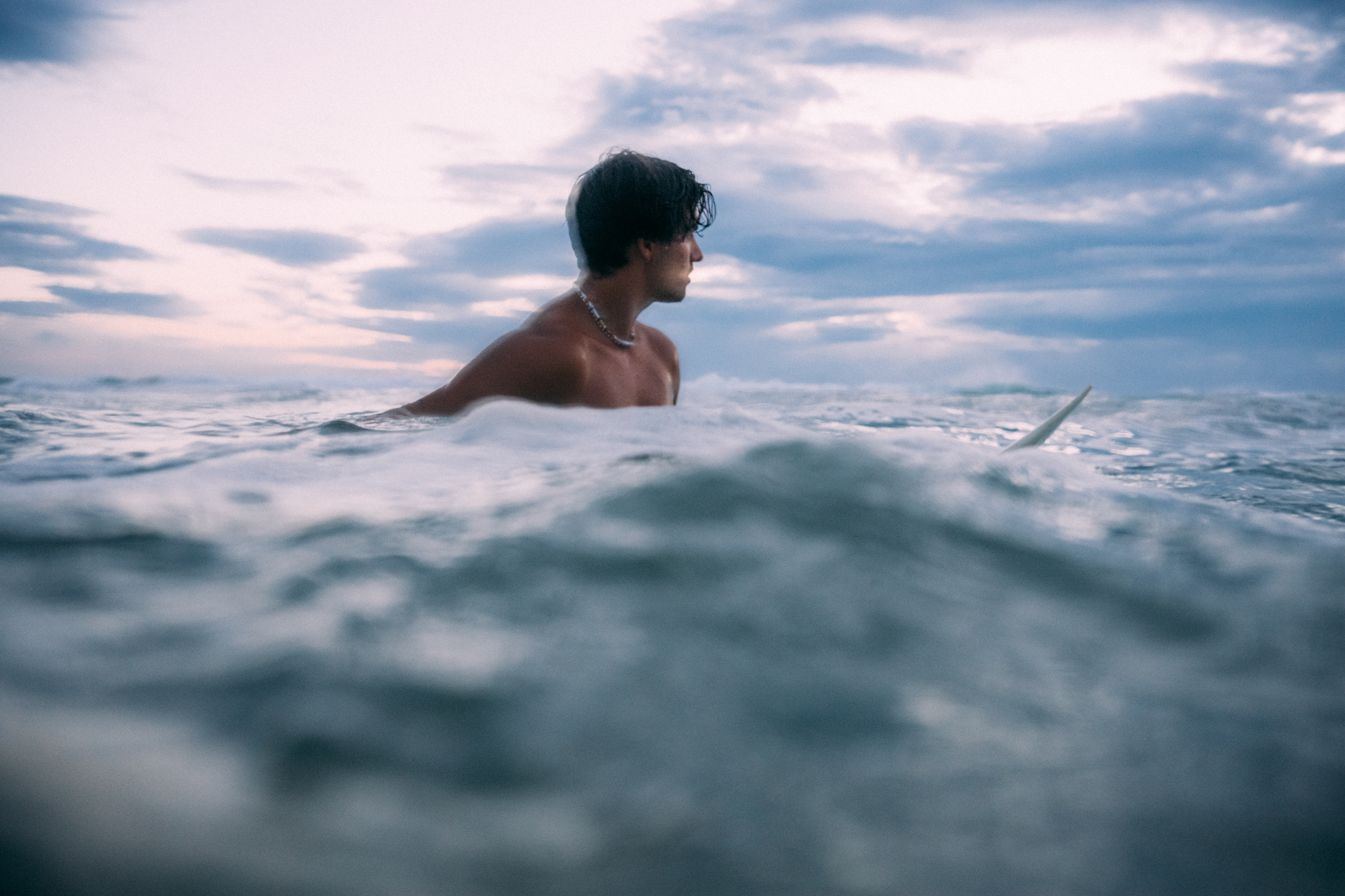 Wellen brechen sanft im letzten Licht des Tages, während ein Surfer in der Blauen Stunde auf dem Wasser wartet.