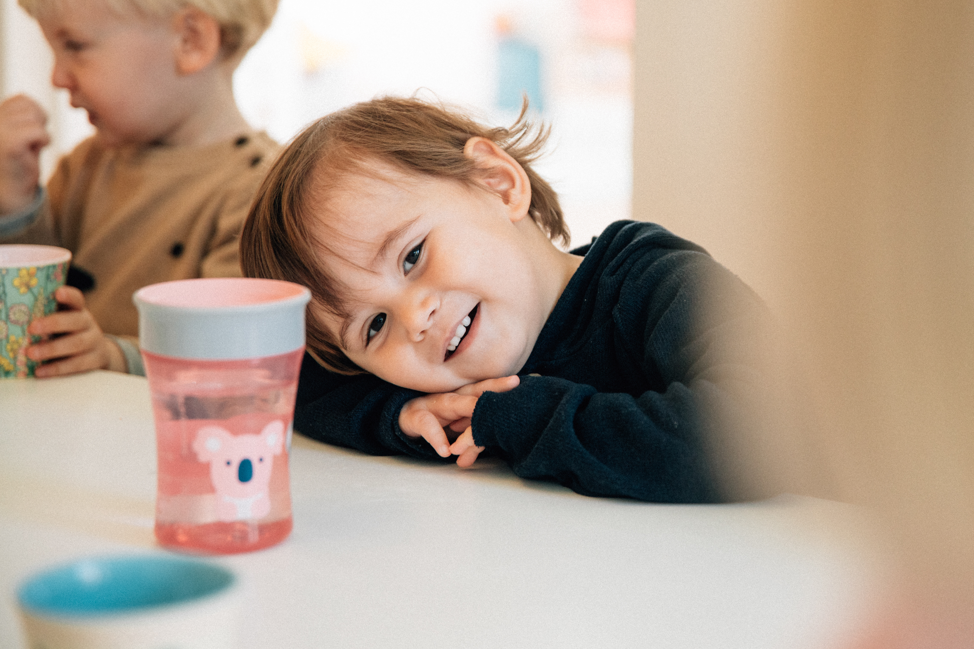 Ein fröhliches Kind sitzt lächelnd am Tisch in der Kindervilla Stuttgart.