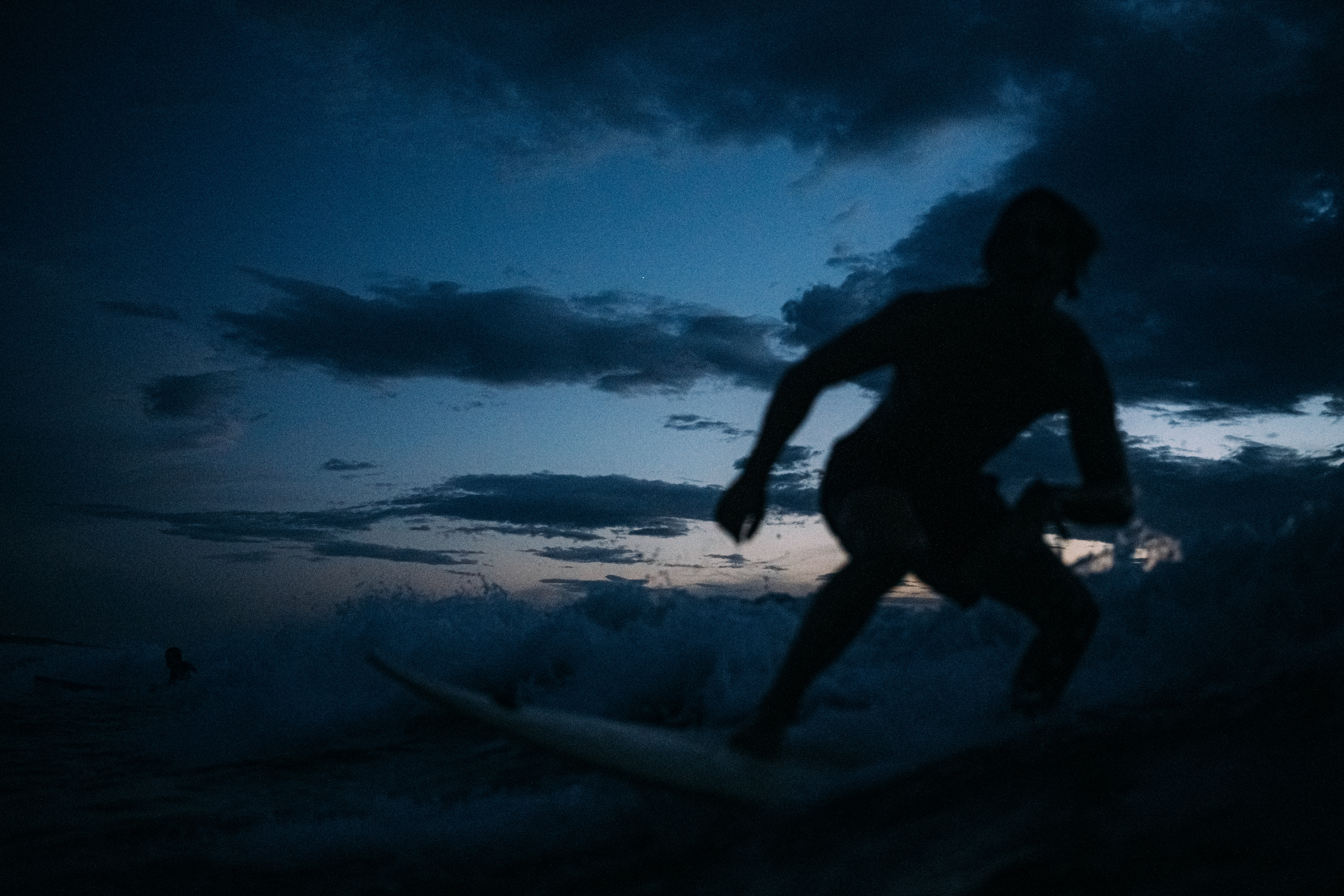 Ein Surfbrett ragt aus dem Wasser, während der Himmel in tiefes Blau übergeht.