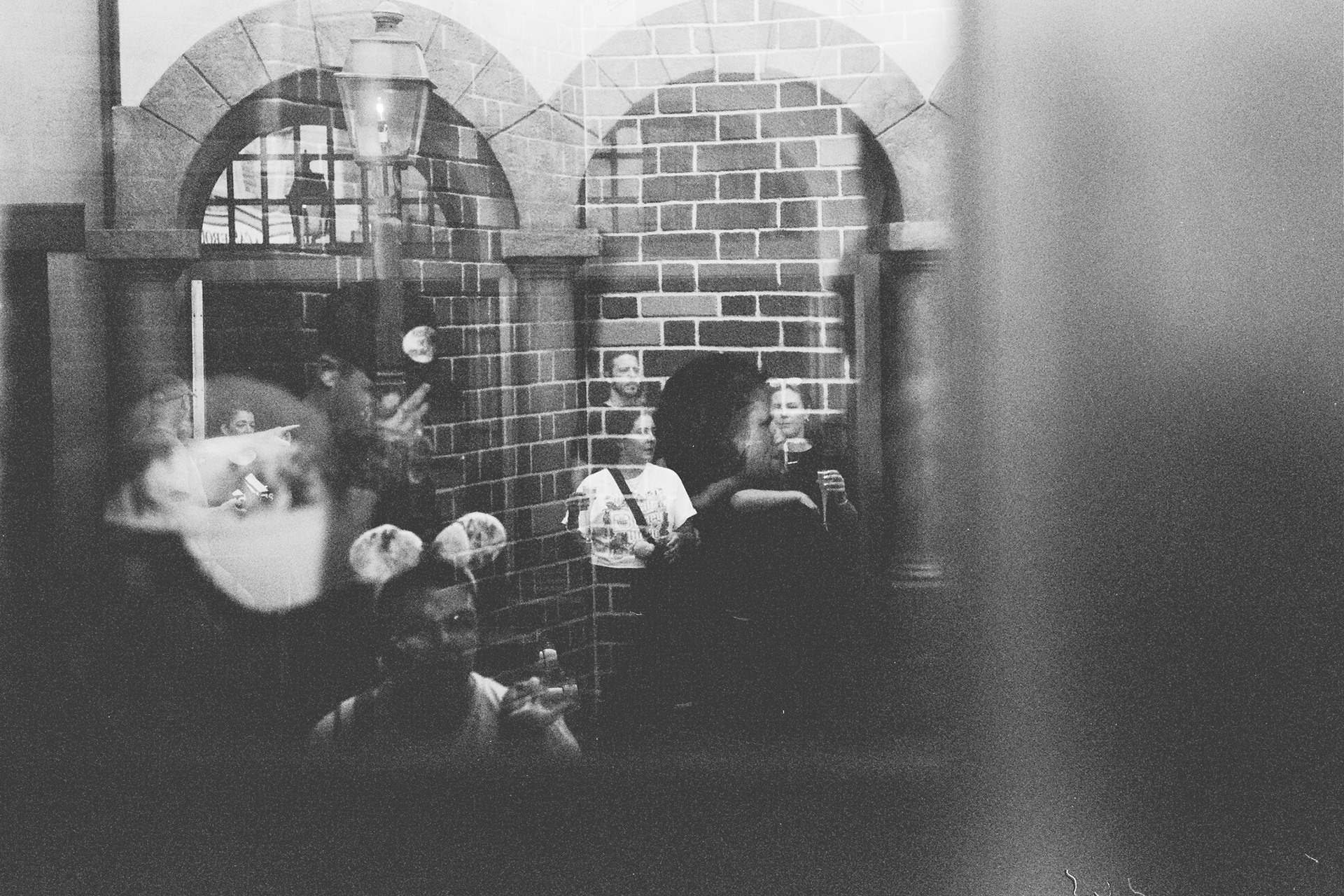Black and white photo of tourists reflected in a window against a brick wall.