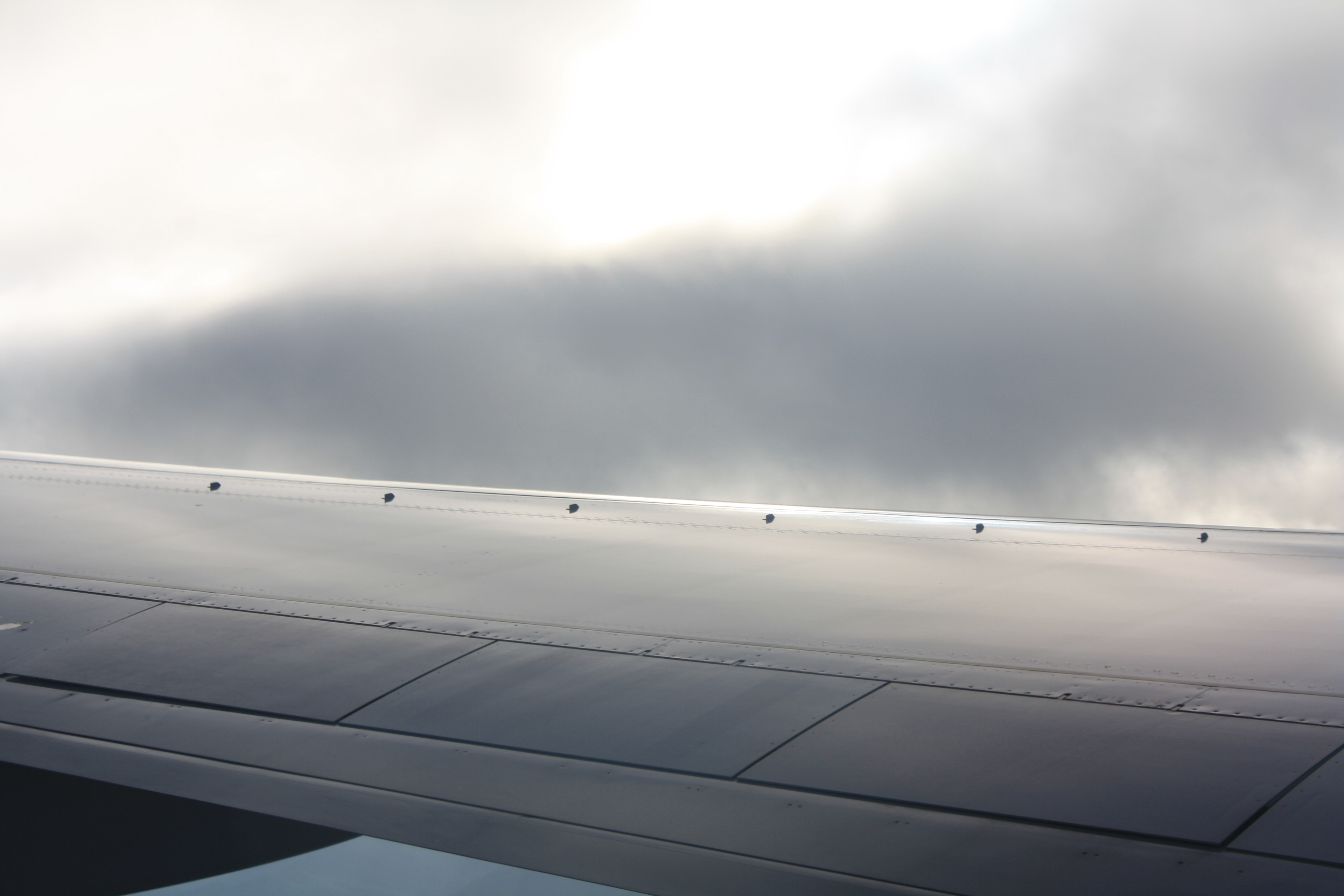 A steel sky reflects off the metal of an airplane wing, which nearly blends in with the clouds.