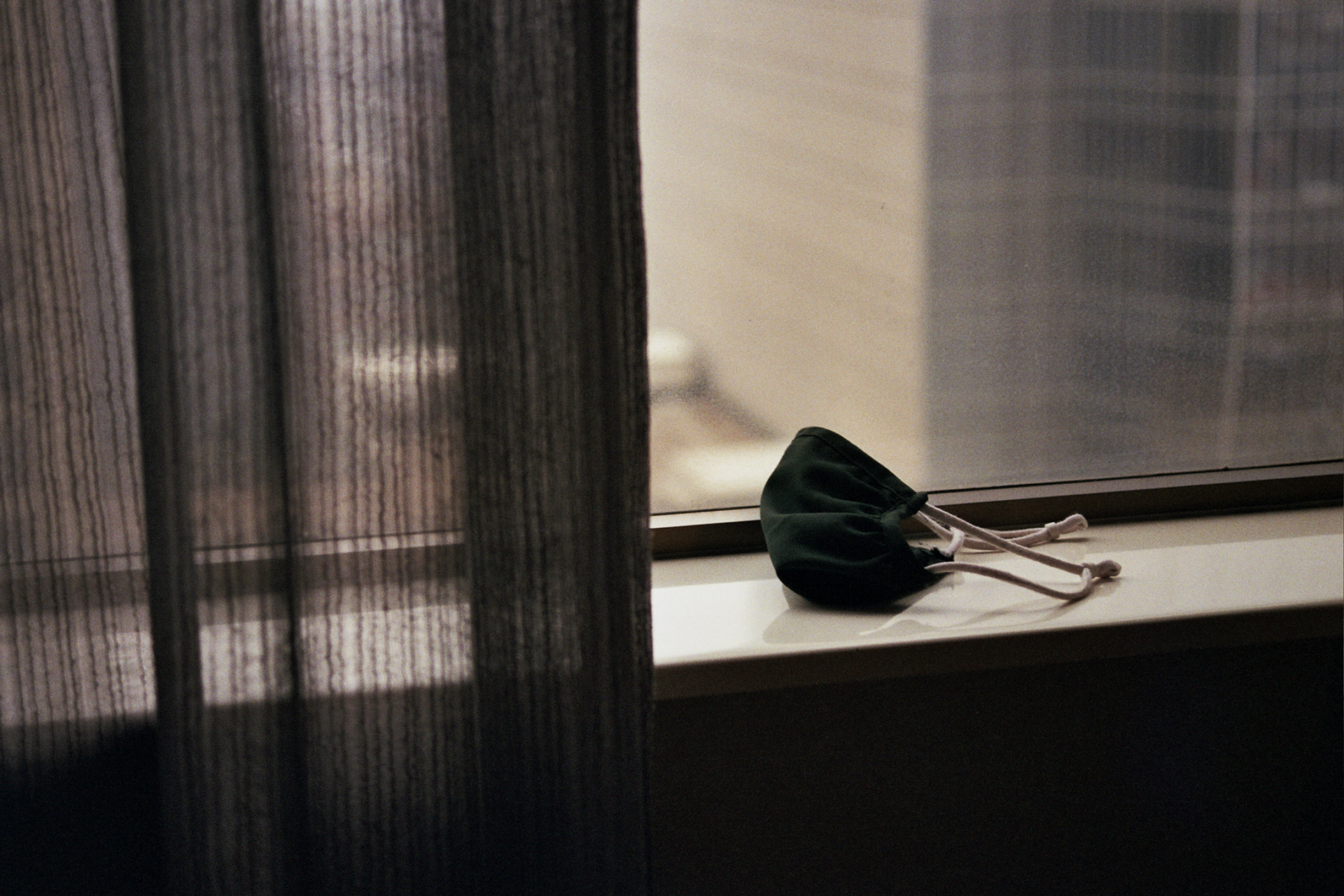 A lonely COVID face mask sits on a windowsill in melancholy light.