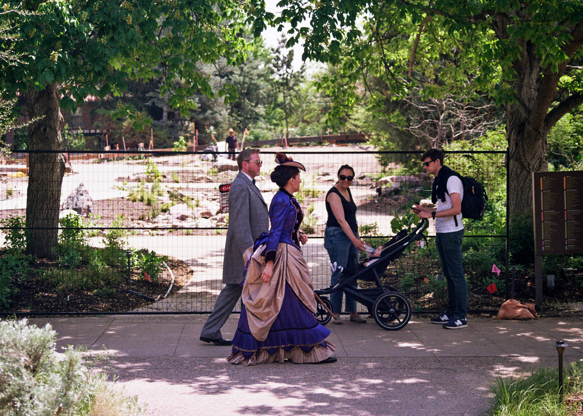Two people dressed in Victorian garb stride past modern onlookers.