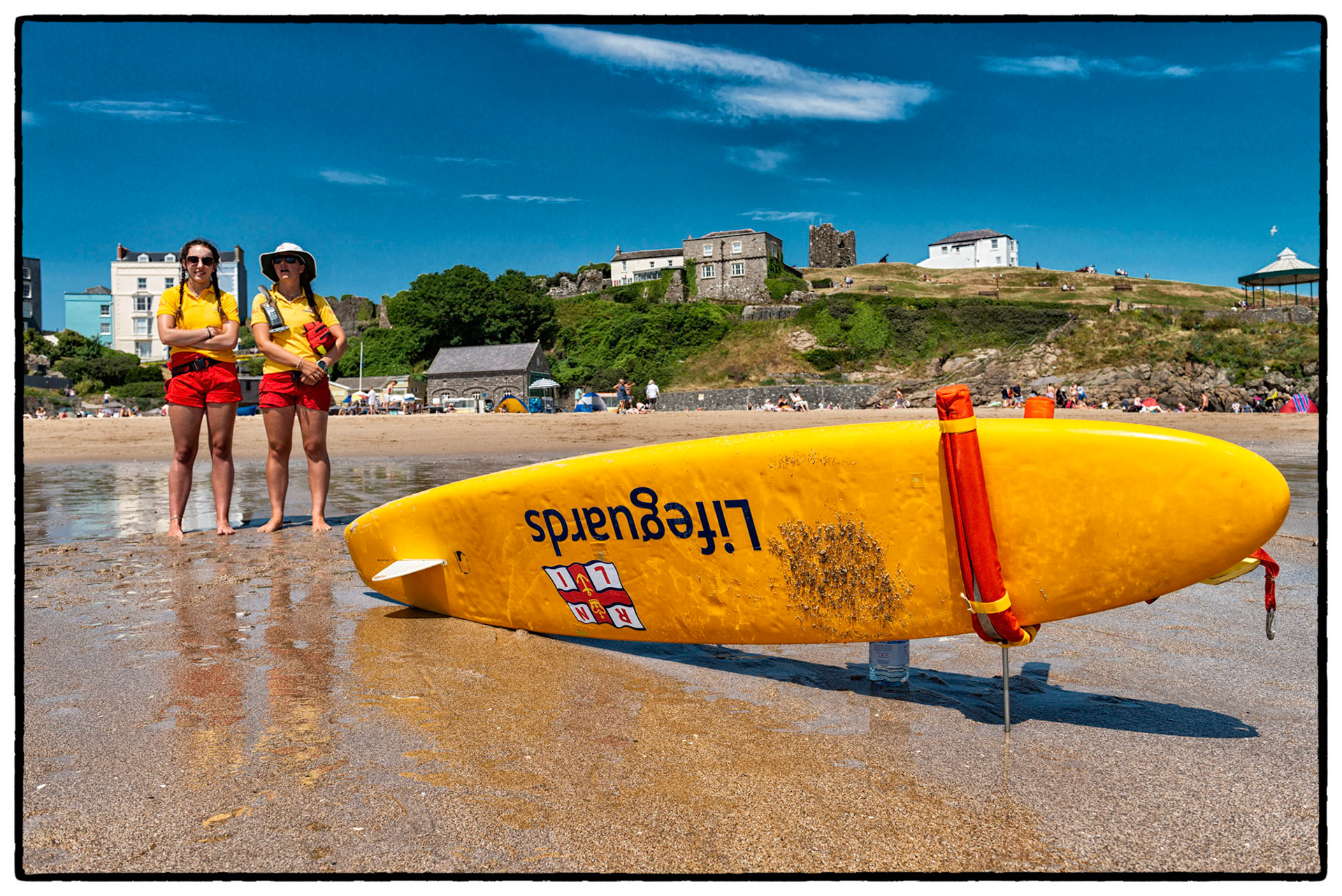 Under blue summer sky the ladies of the Tenby RNLI Lifeguards watch over holidaymakers on Castle Beach in the pretty seaside town of Tenby, Pembrokeshire, Wales, UK.