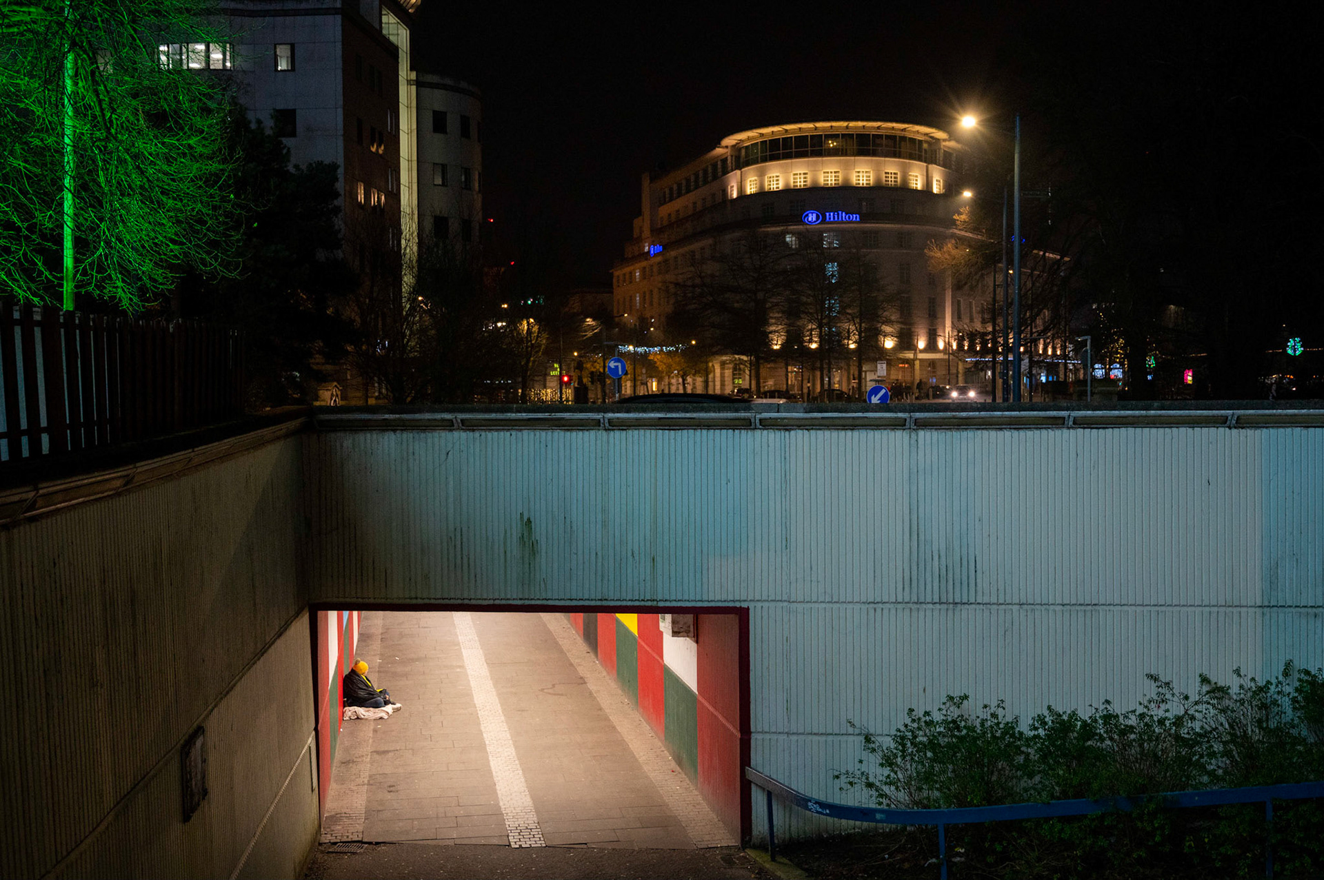Two sides to a city. Homelessness alongside affluence, a common site in most UK cities these days. Here in Cardiff the homeless issue seems worse than ever with evidence all around the city centre.In this picture on a freezing cold December night in the shadow of the festive Winter Wonderland and only a stones throw from City Hall a homeless person sits wrapped in blankets in an underpass against the backdrop of one of the many upmarket city centre hotels as.