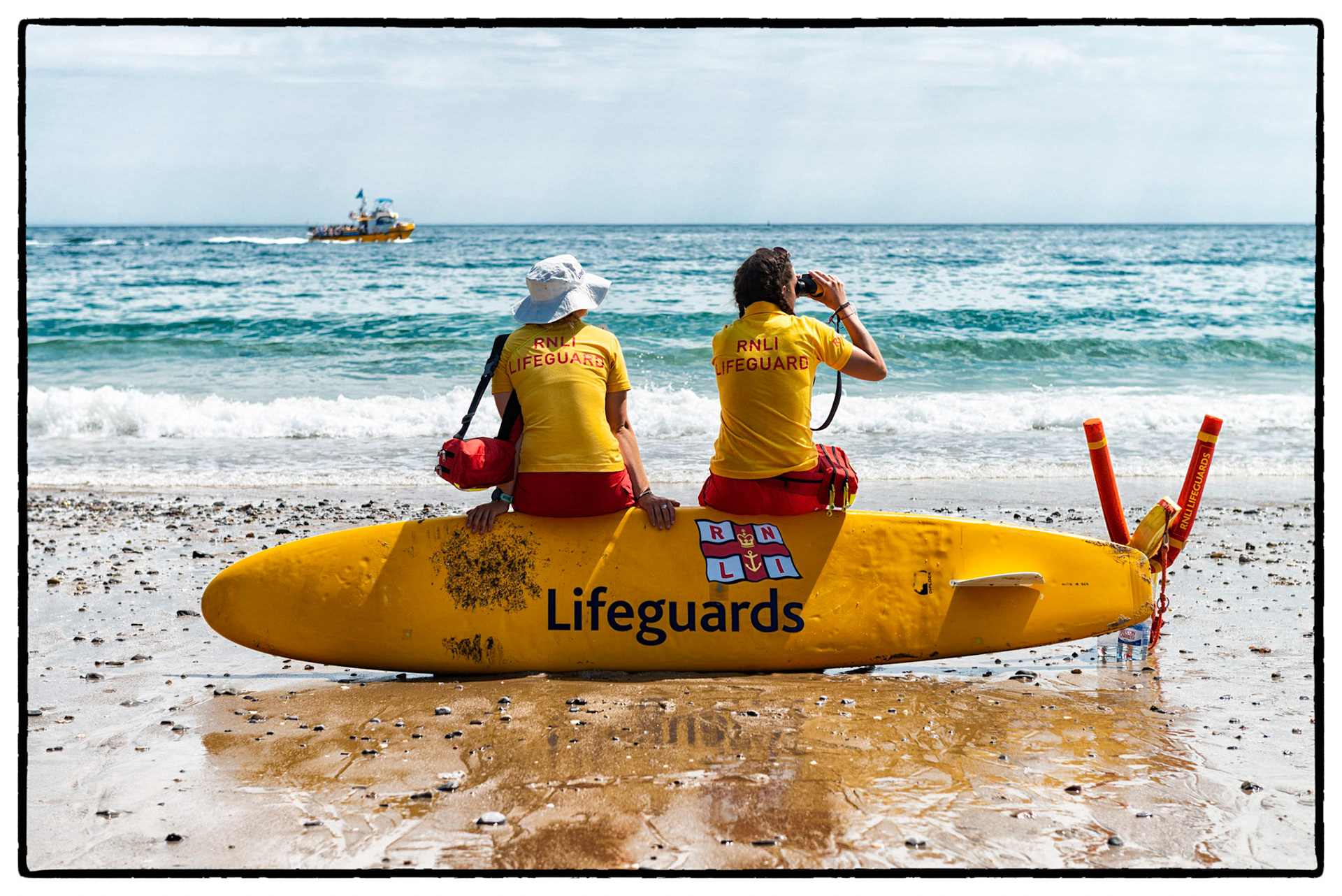 Under blue summer sky the ladies of the Tenby RNLI Lifeguards watch over holidaymakers on Castle Beach in the pretty seaside town of Tenby, Pembrokeshire, Wales, UK.