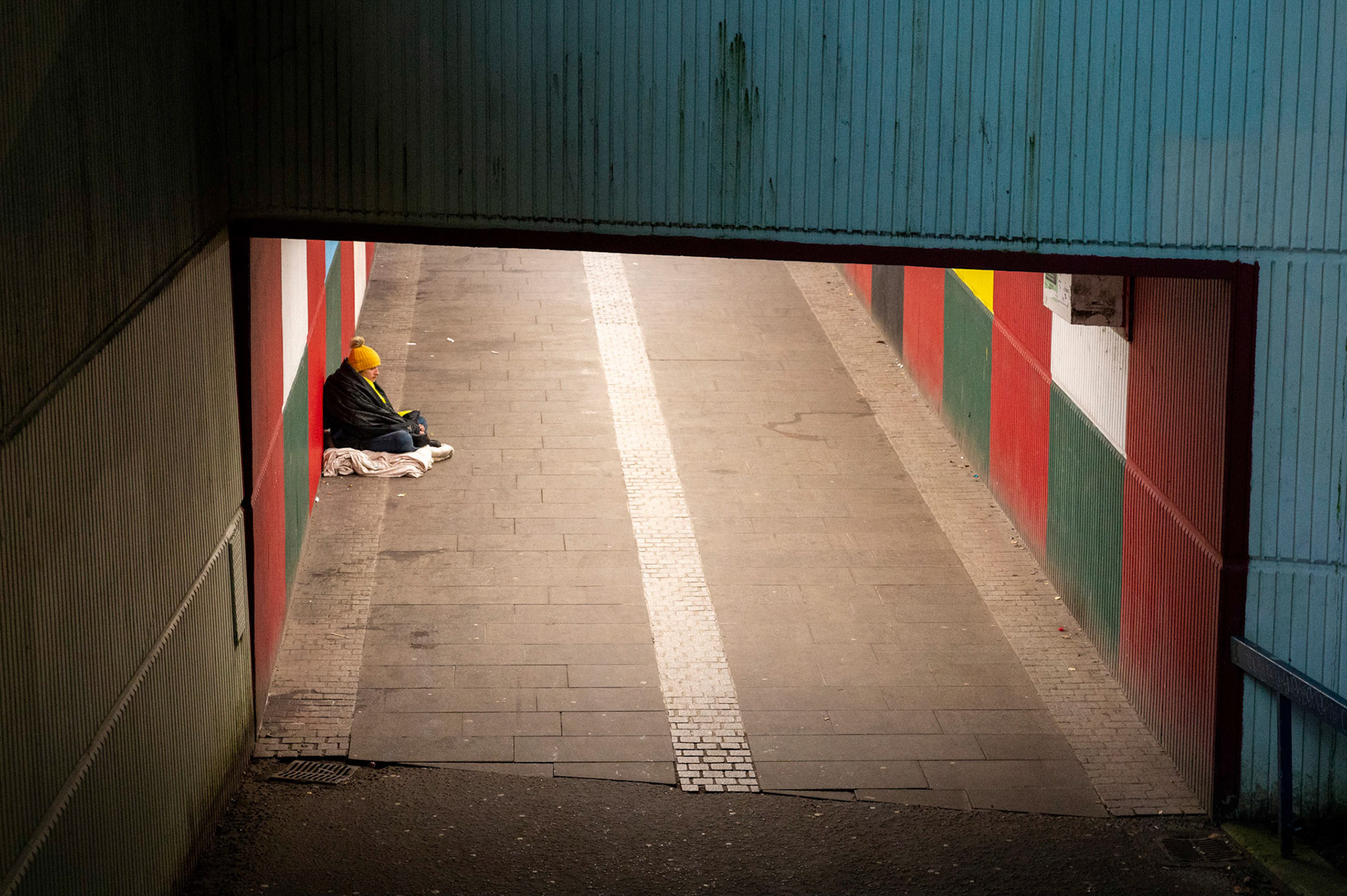 Two sides to a city. Homelessness alongside affluence, a common site in most UK cities these days. Here in Cardiff the homeless issue seems worse than ever with evidence all around the city centre.In this picture on a freezing cold December night in the shadow of the festive Winter Wonderland and only a stones throw from City Hall a homeless person sits wrapped in blankets in an underpass against the backdrop of one of the many upmarket city centre hotels as.