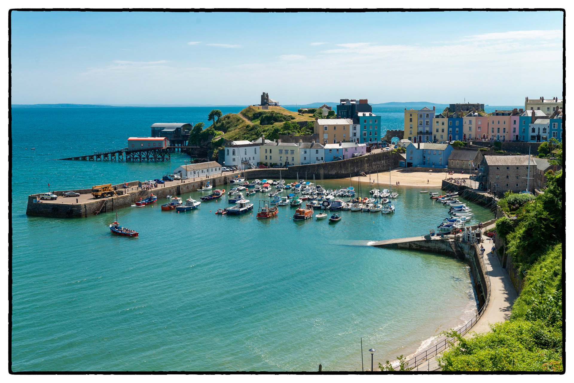 The pretty seaside town of Tenby, Pembrokeshire, Wales, UK looks stunning under a blue summer sky. Colourful  houses surround the harbour at high tide