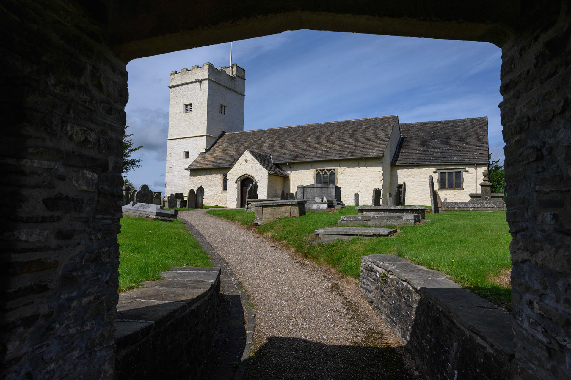 St Sannan’s Church and graveyard, Bedwellty, South Wales, UK against a blue summer sky, viewed through the lichgate.
