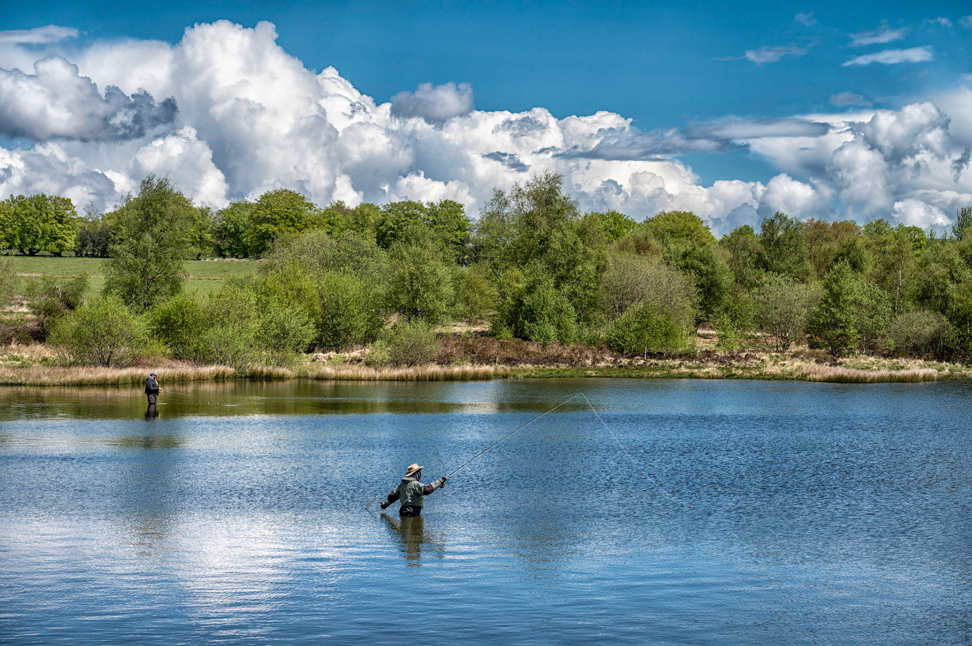 Fly fishing at Penyfan Pond, near Blackwood, South Wales against cloudy blue sky.