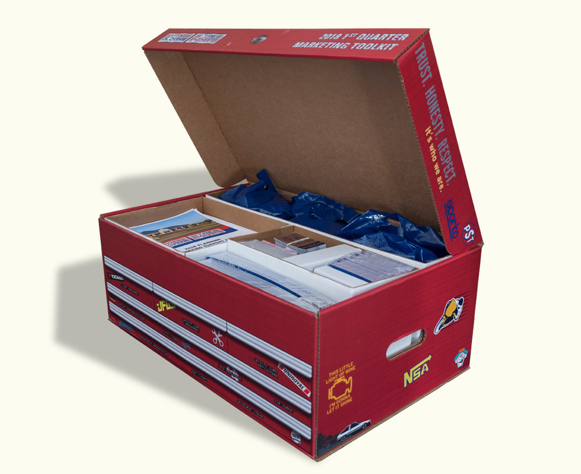 Red marketing toolbox for Express Oil Change. A red cardboard box is designed to look like a mechanic's toolbox that is covered in stickers. Inside, stacks of marketing materials are organized into different compartments.