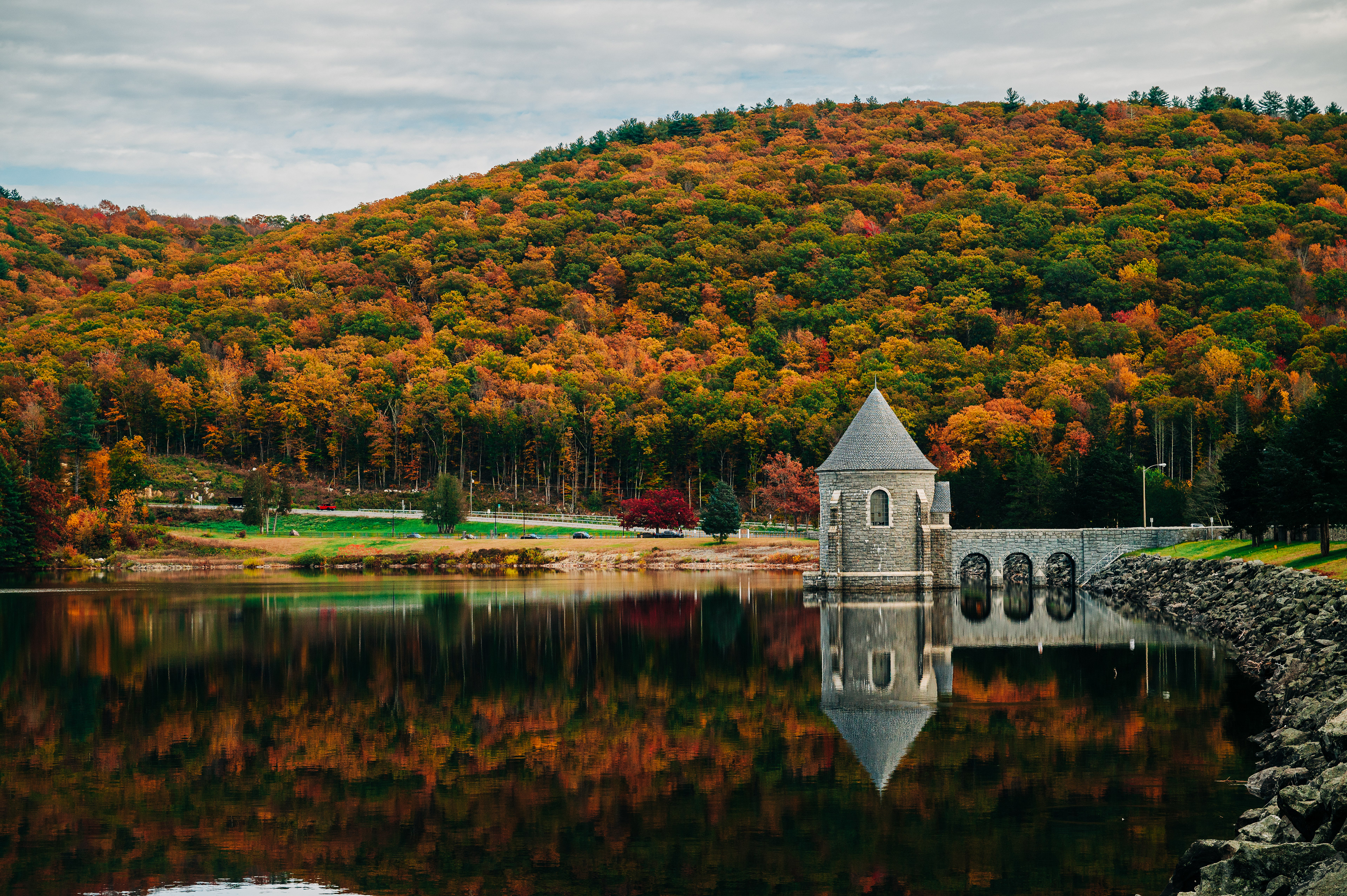   A sandy beach path leading to calm waters, with sparse grass and cloudy skies. 