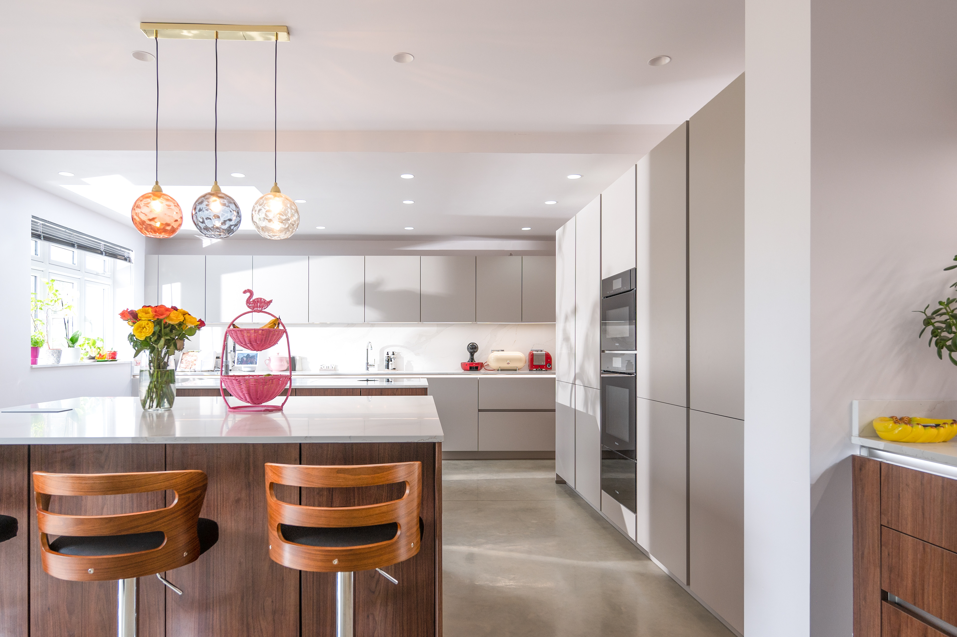 A bright and sunny photograph of a kitchen with modern looking light grey and wooden cupboards.