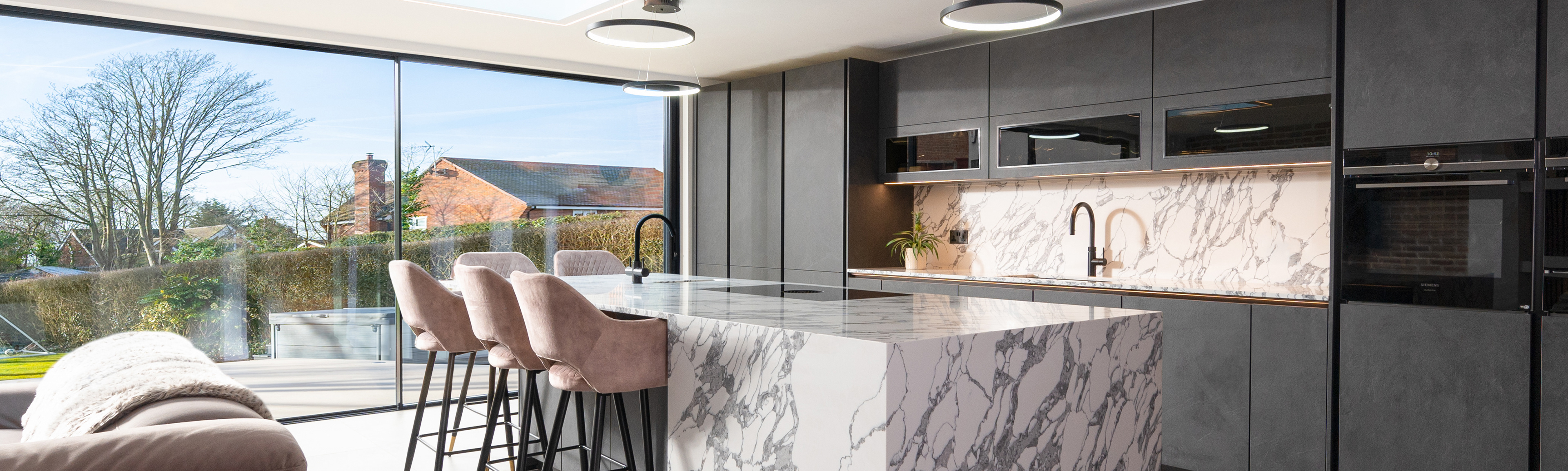 Photograph of a kitchen with modern charcoal grey kitchen units  and white and grey marble worktops.