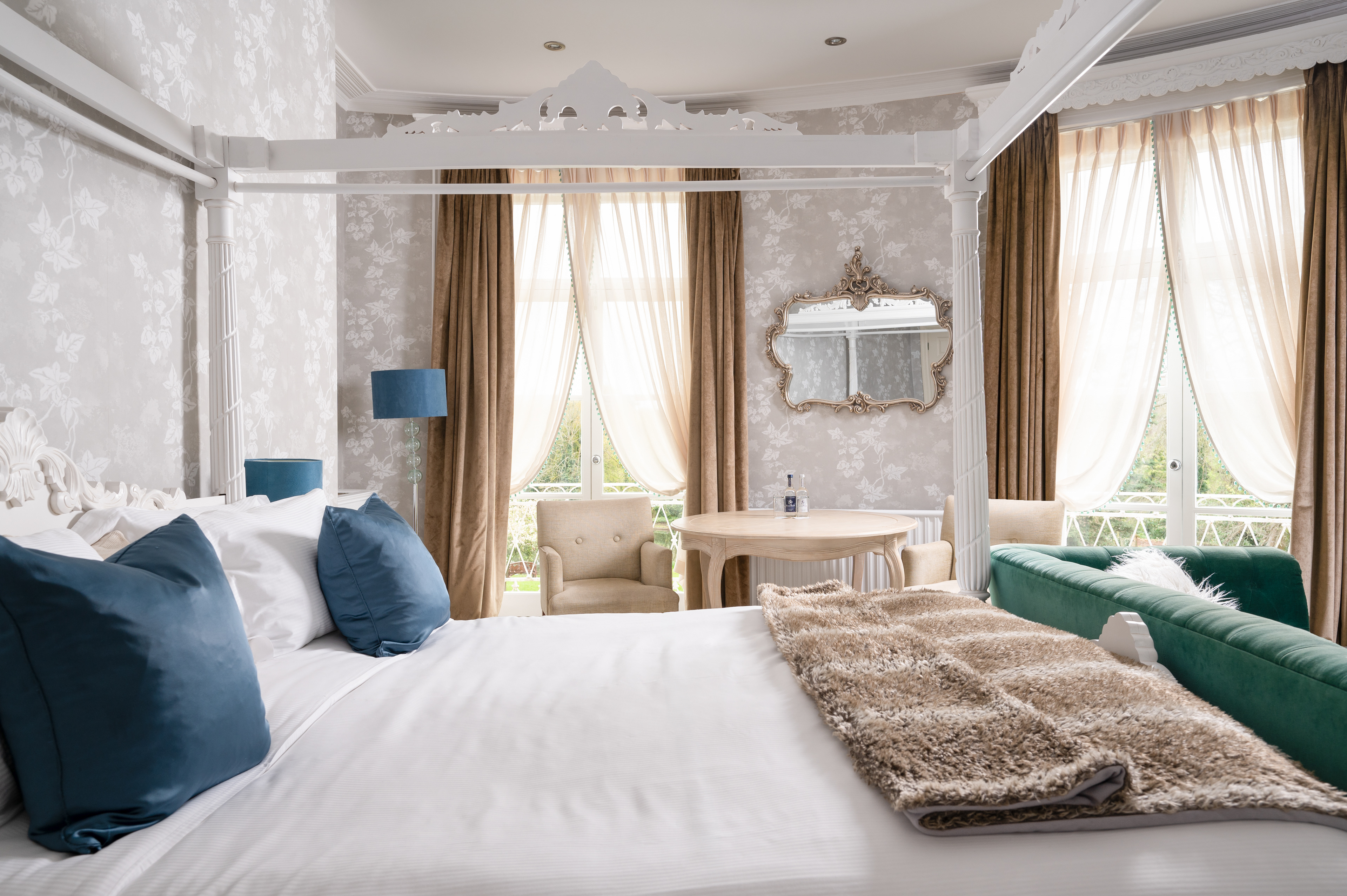 The bridal suite at St Michael's Manor hotel in St Albans featuring a four poster bed a green velvet sofa and a table and chairs.