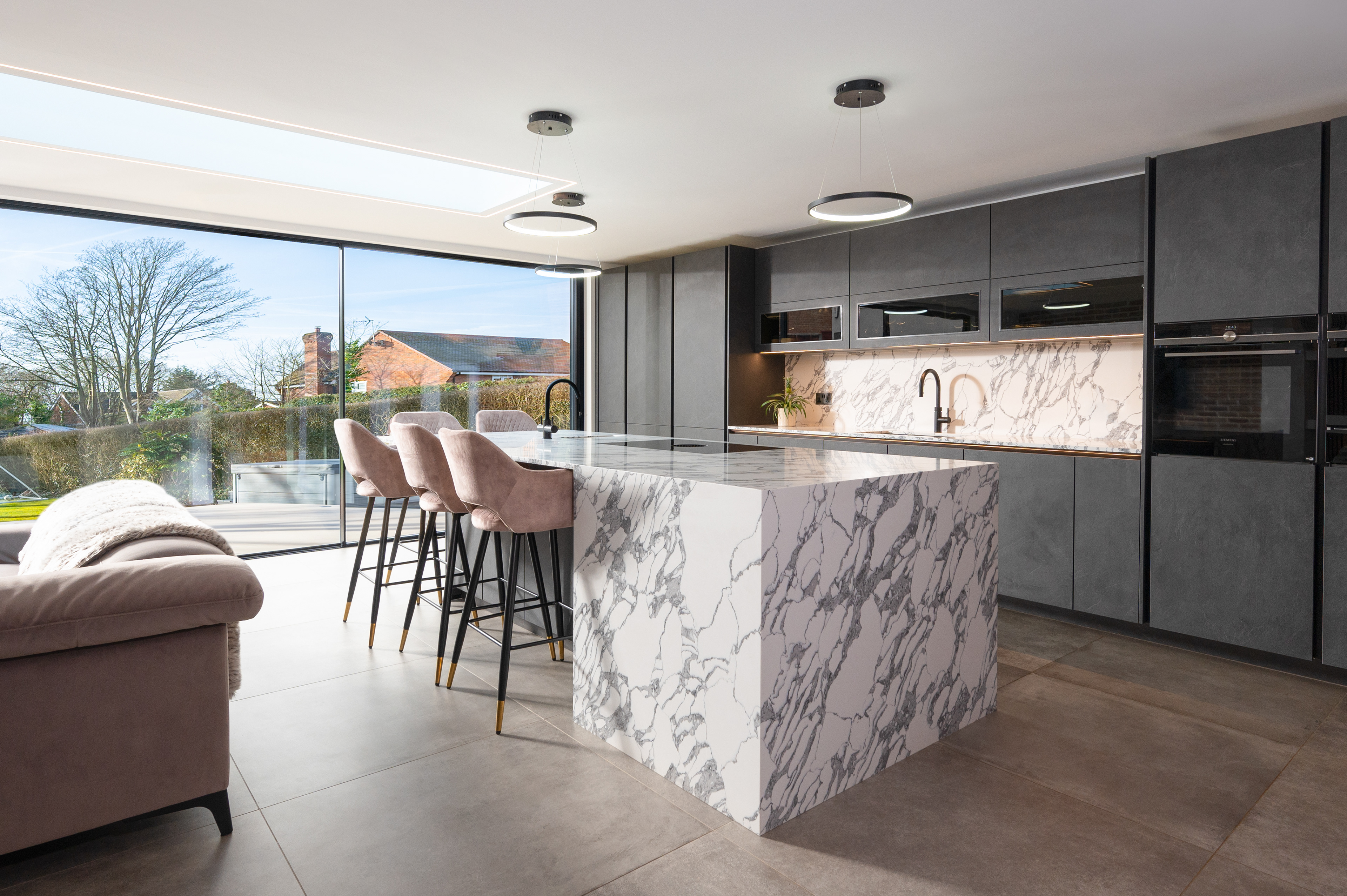 Photograph of a kitchen with modern charcoal grey kitchen units  and white and grey marble worktops.