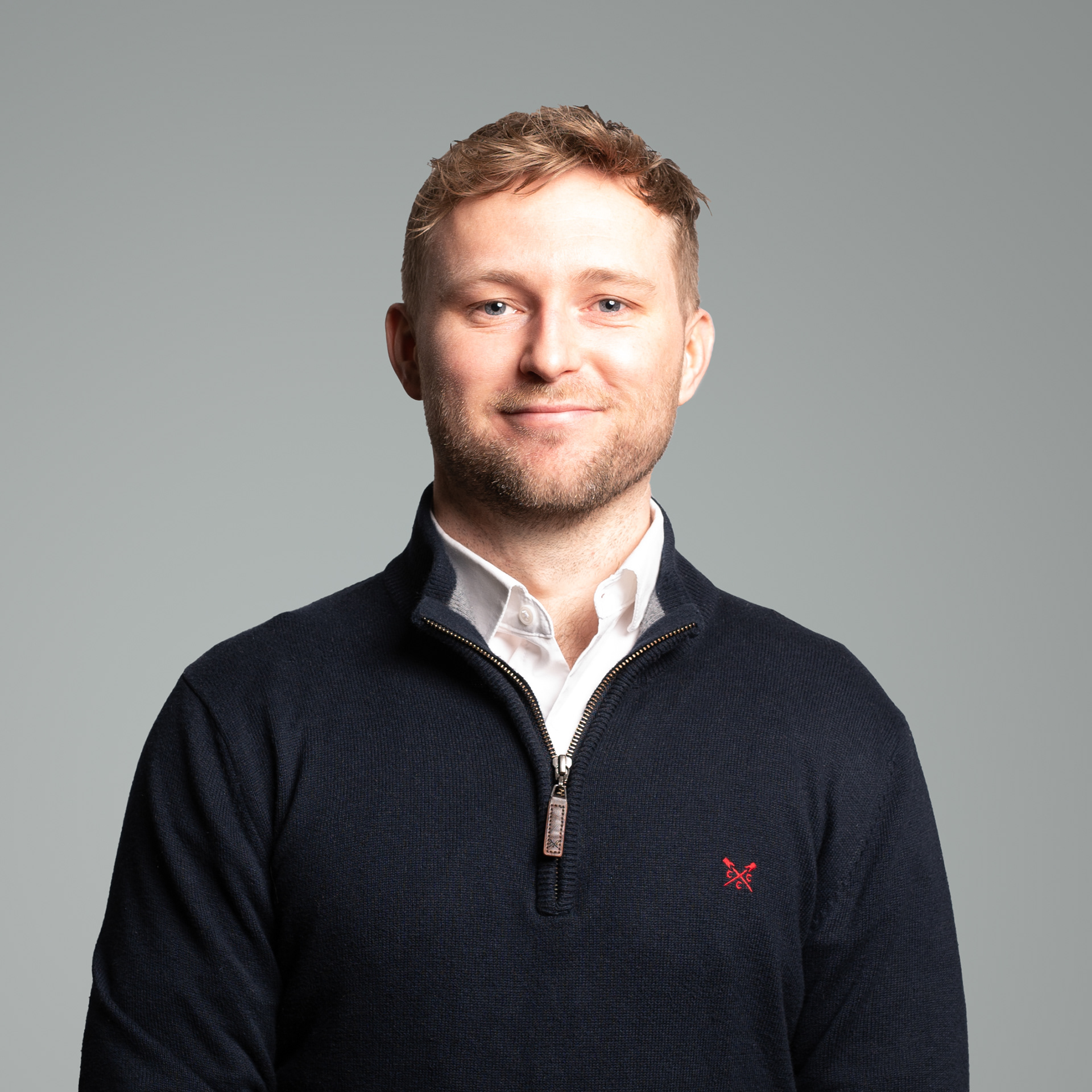 Portrait photograph of a young man wearing a white shirt and a blue jumper set against a grey background