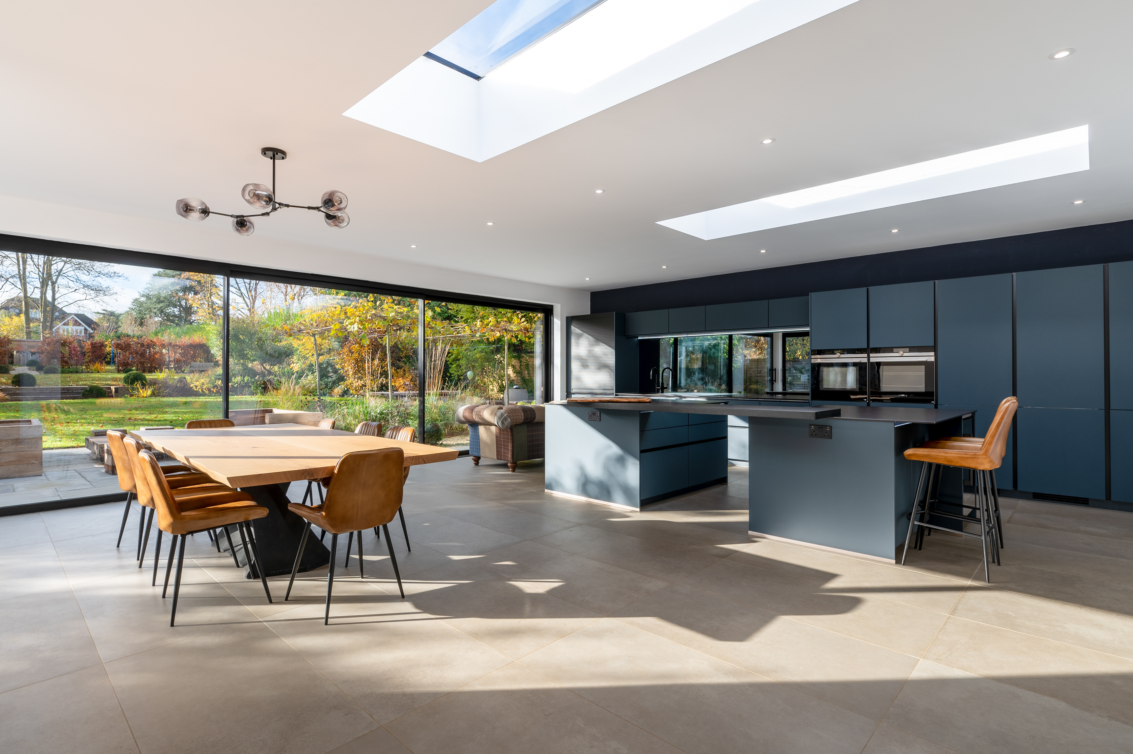 A kitchen and dining area with large sliding doors to the garden. The kitchen is a modern design in a dark blue colour.
