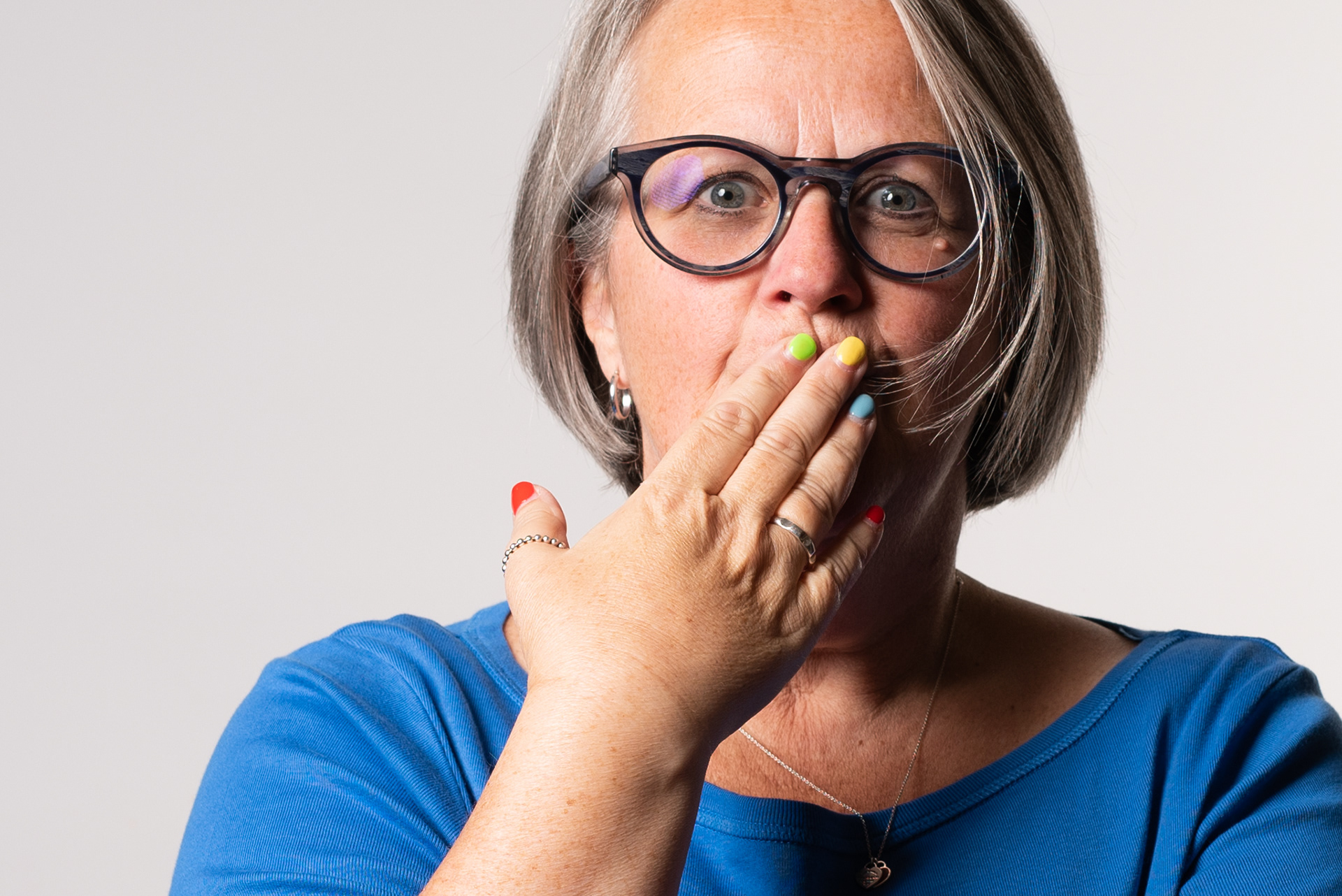 Portrait of a woman with glasses and a bob haircut. Her hand is over her mouth and she has brightly painted finger nails.