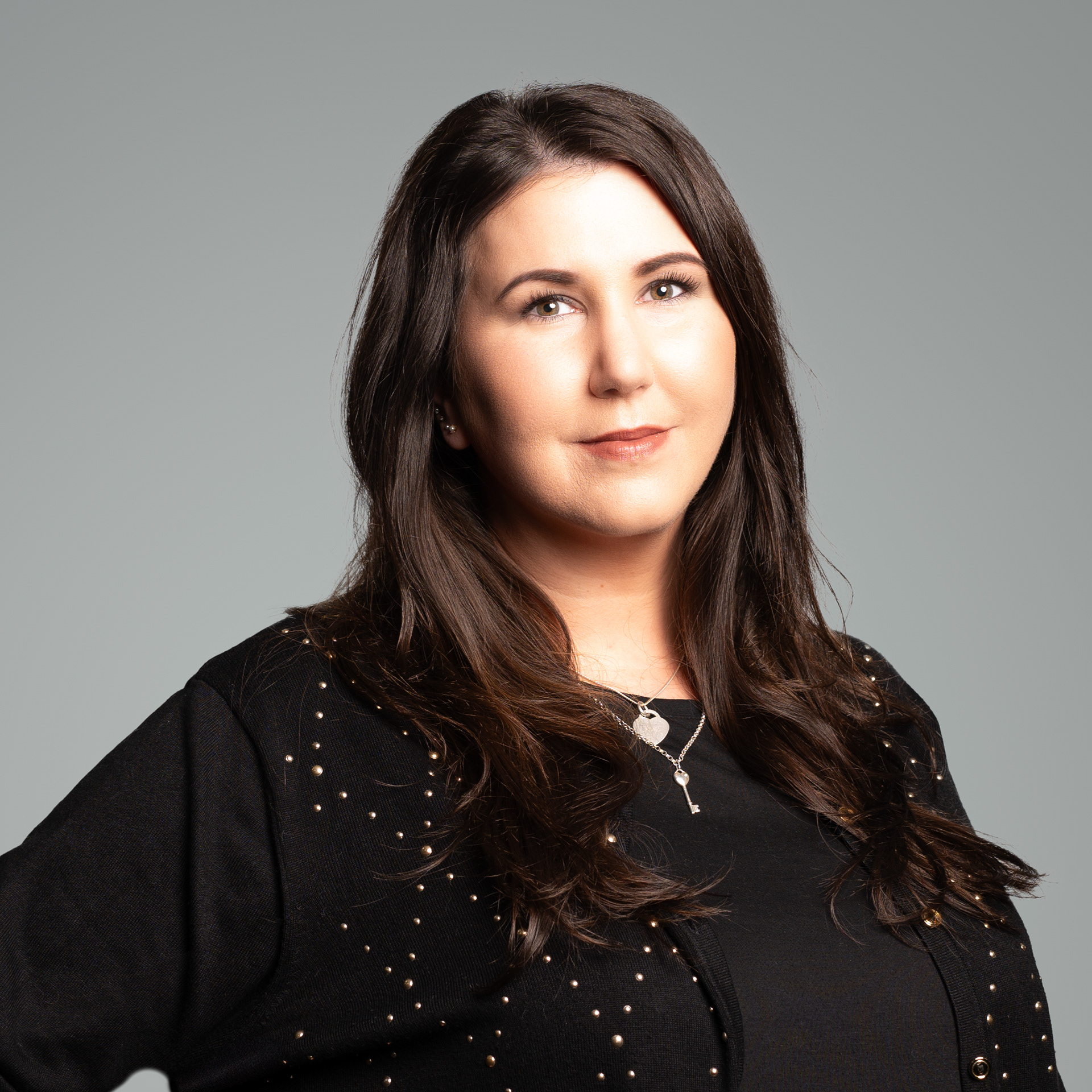Portrait photograph of a young woman with long black hair wearing a black t-shirt and cardigan set against a grey background