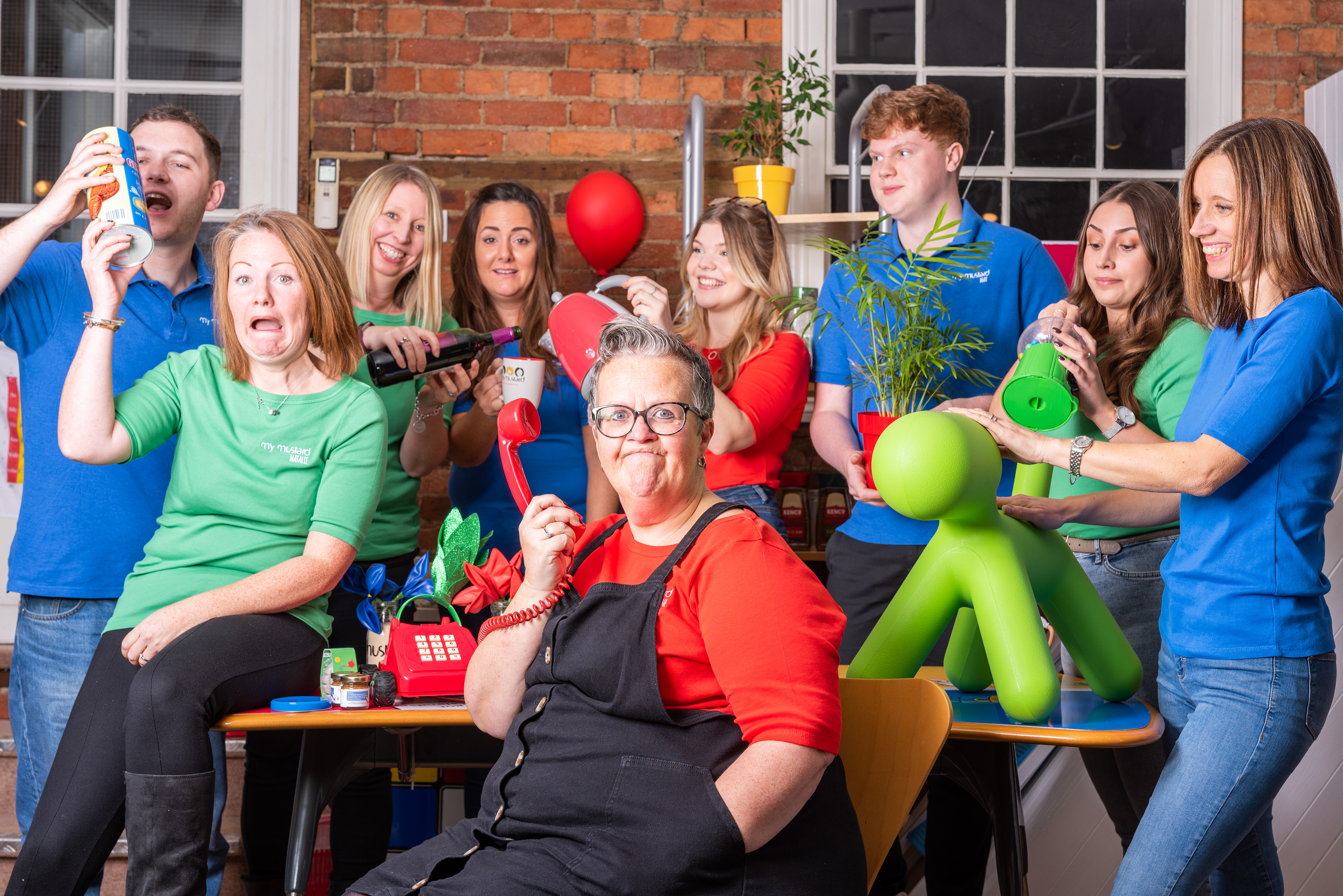 A business portrait of nine people wearing brightly coloured t-shirts