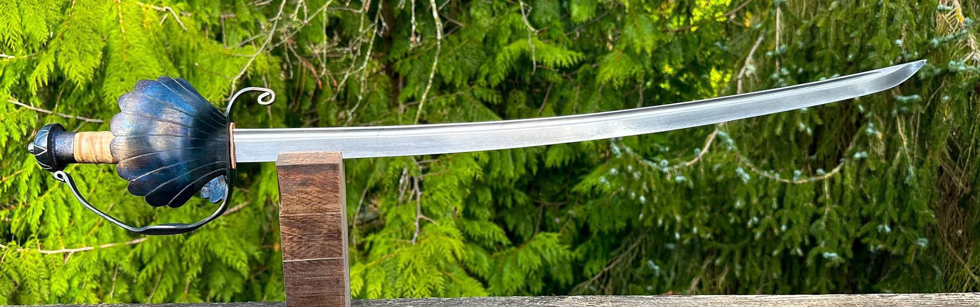 Triple Shell Cutlass. Blade is 5160, with a guard forged out of a single sheet of 12 gauge steel. Engraved pommel with a fluted maple grip handle.