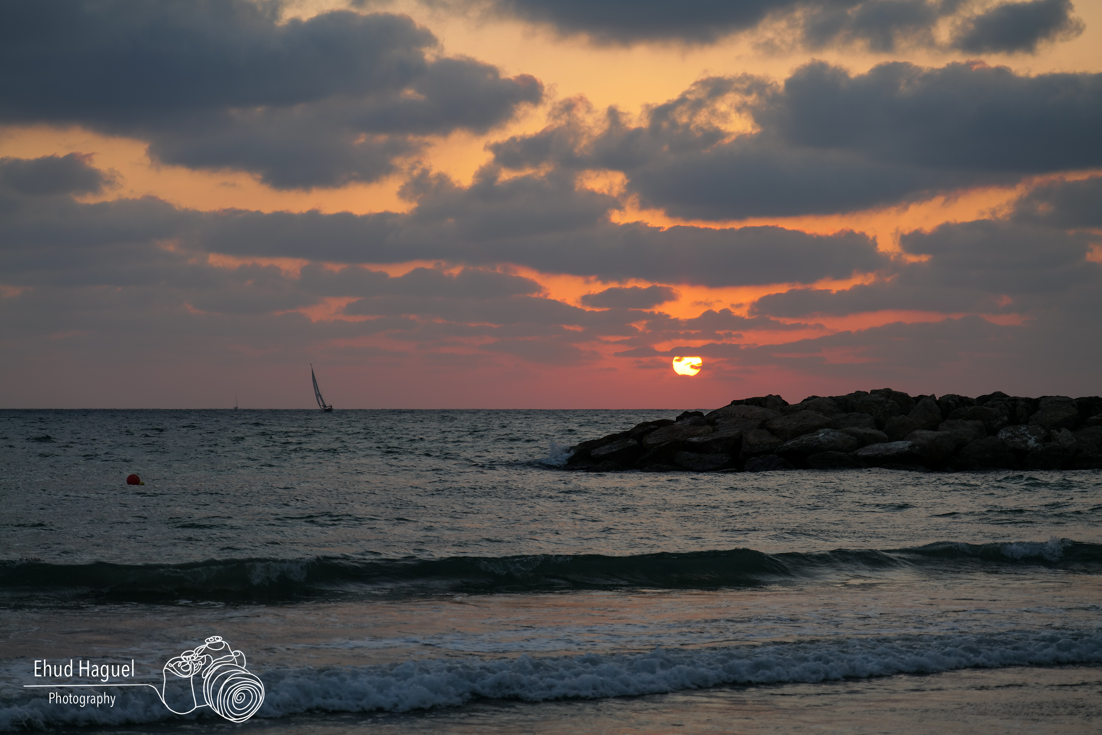 Sunset over Mediterranean sea with sailboat and rocky shore, Israel