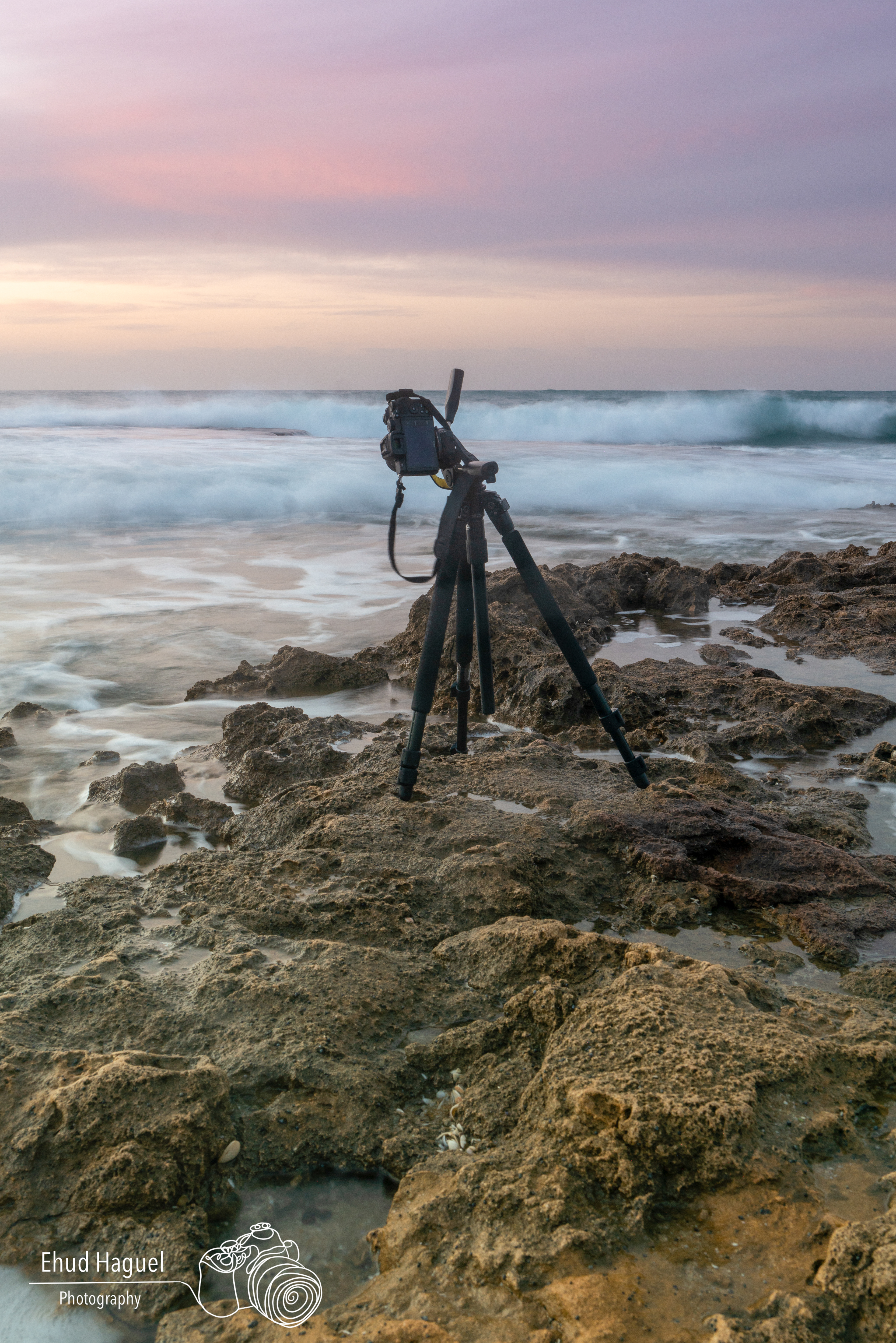 Camera on tripod at rocky shoreline during sunset, long exposure photography Israel